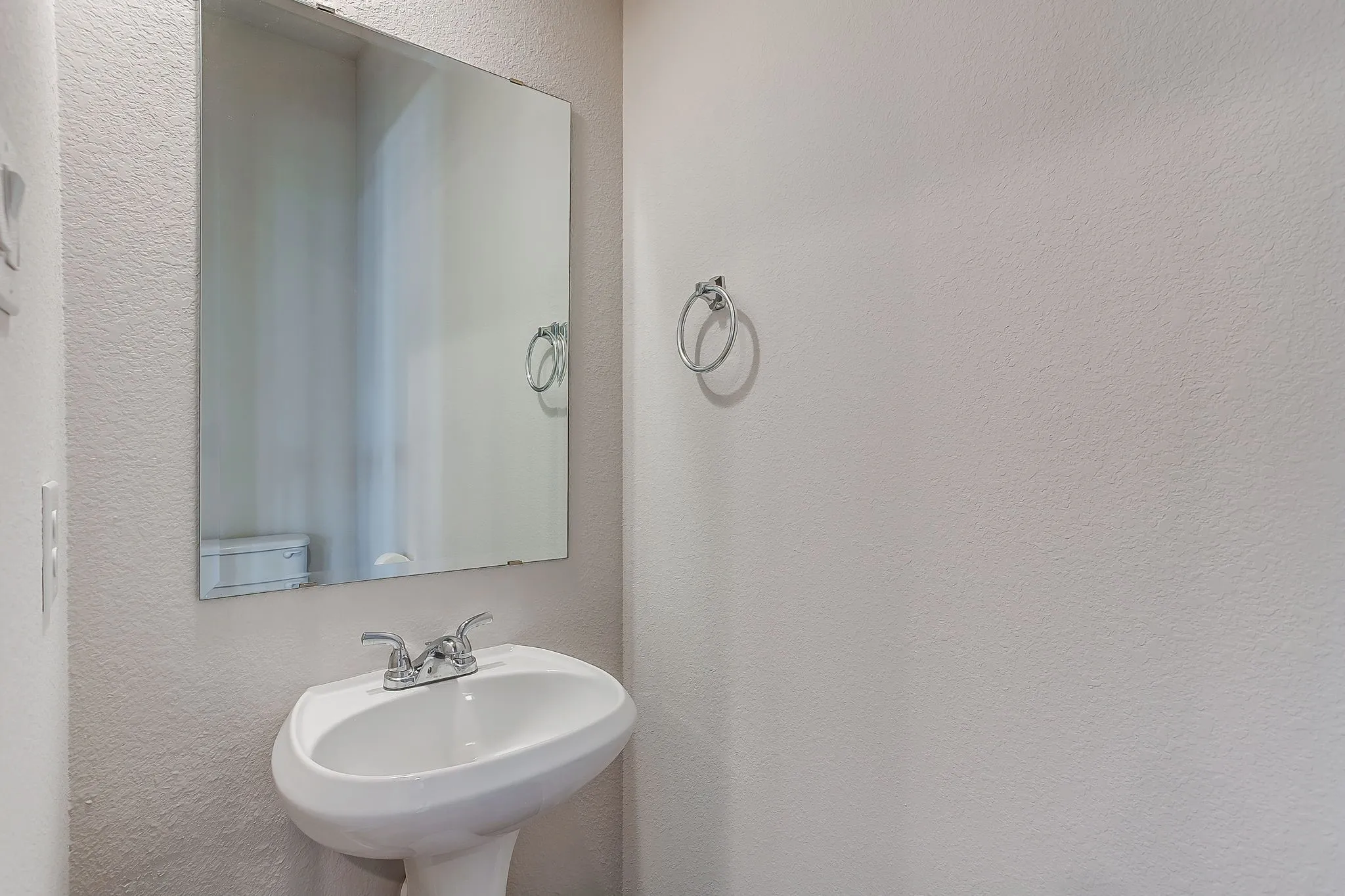 Pedestal sink with chrome faucet, large wall mirror, and chrome towel ring