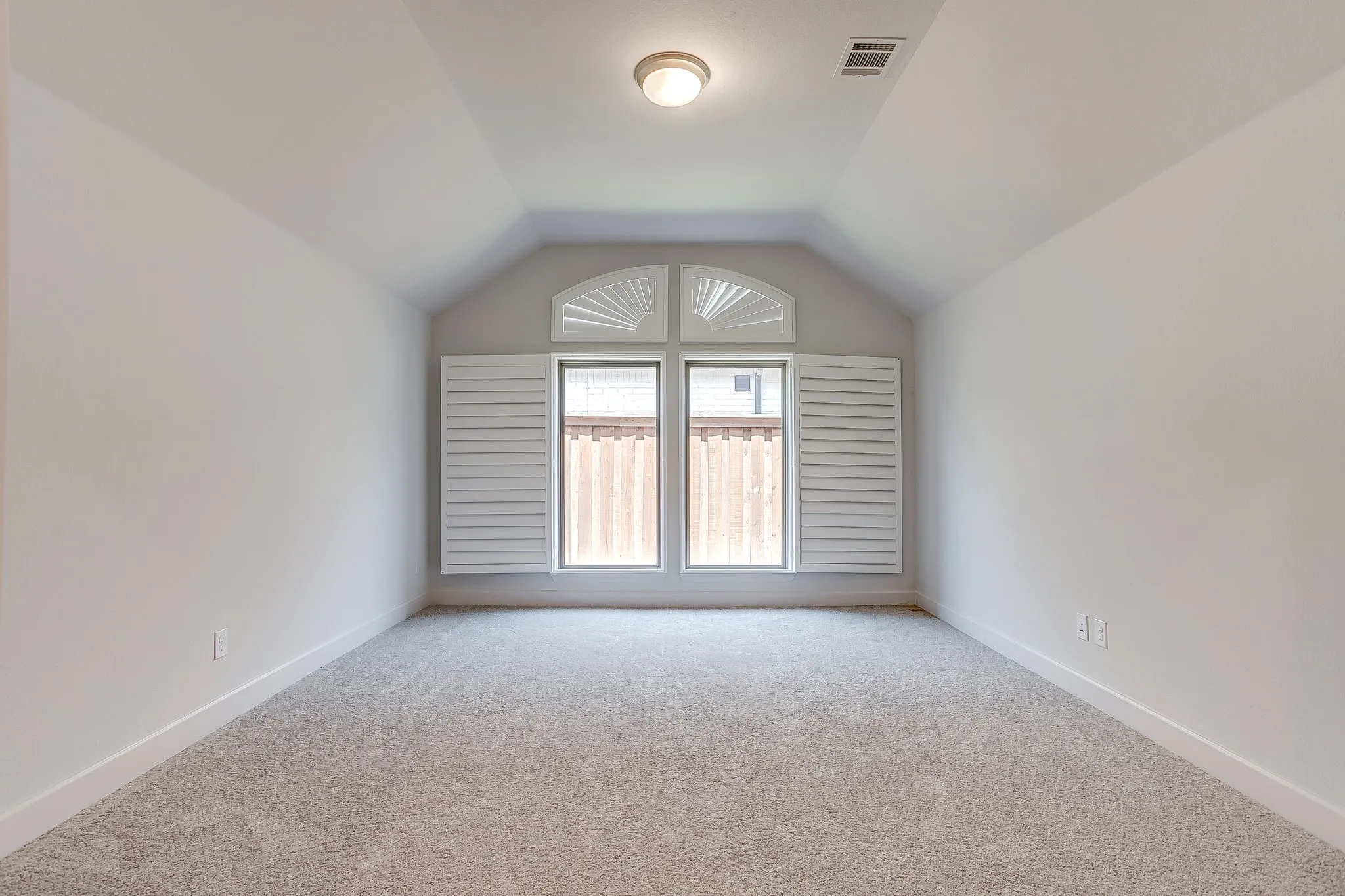Carpeted room featuring a double window with white plantation shutters and an arched transom window