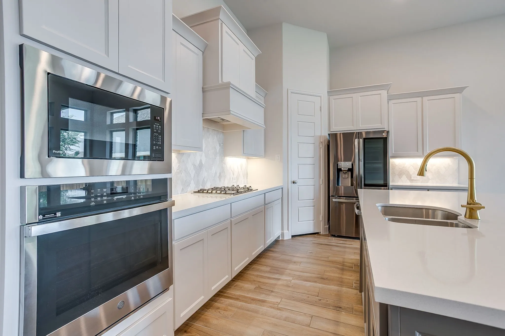 Modern kitchen featuring built-in stainless steel appliances, light wood-finish flooring, white shaker-style cabinetry, and white countertops