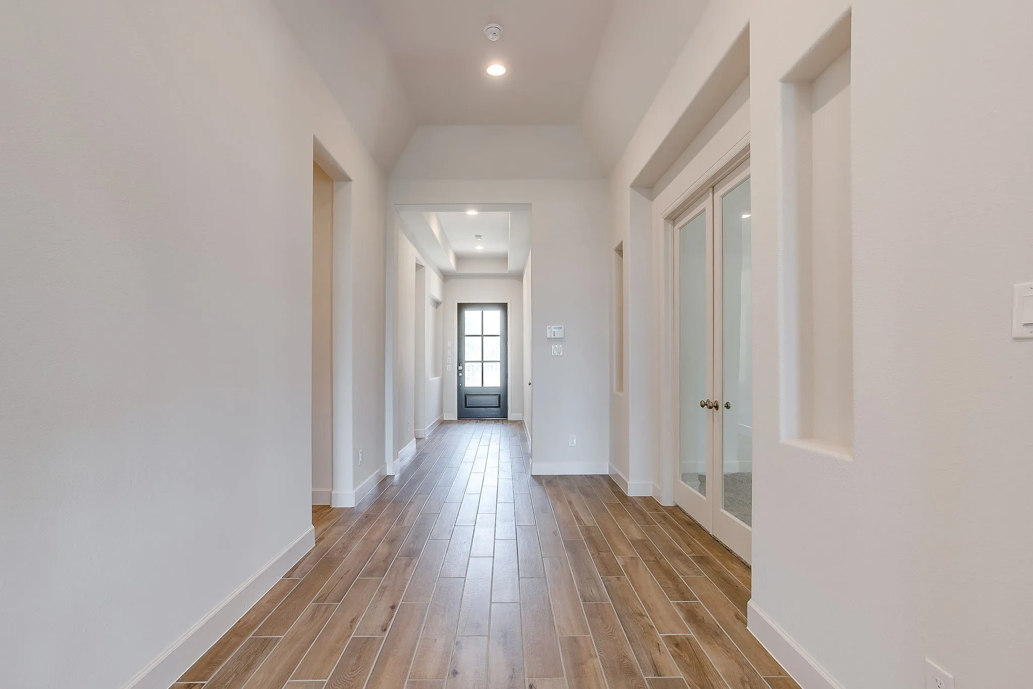 Long hallway featuring wood-finish flooring, recessed lighting, white walls, and a decorative front door with multiple window panes