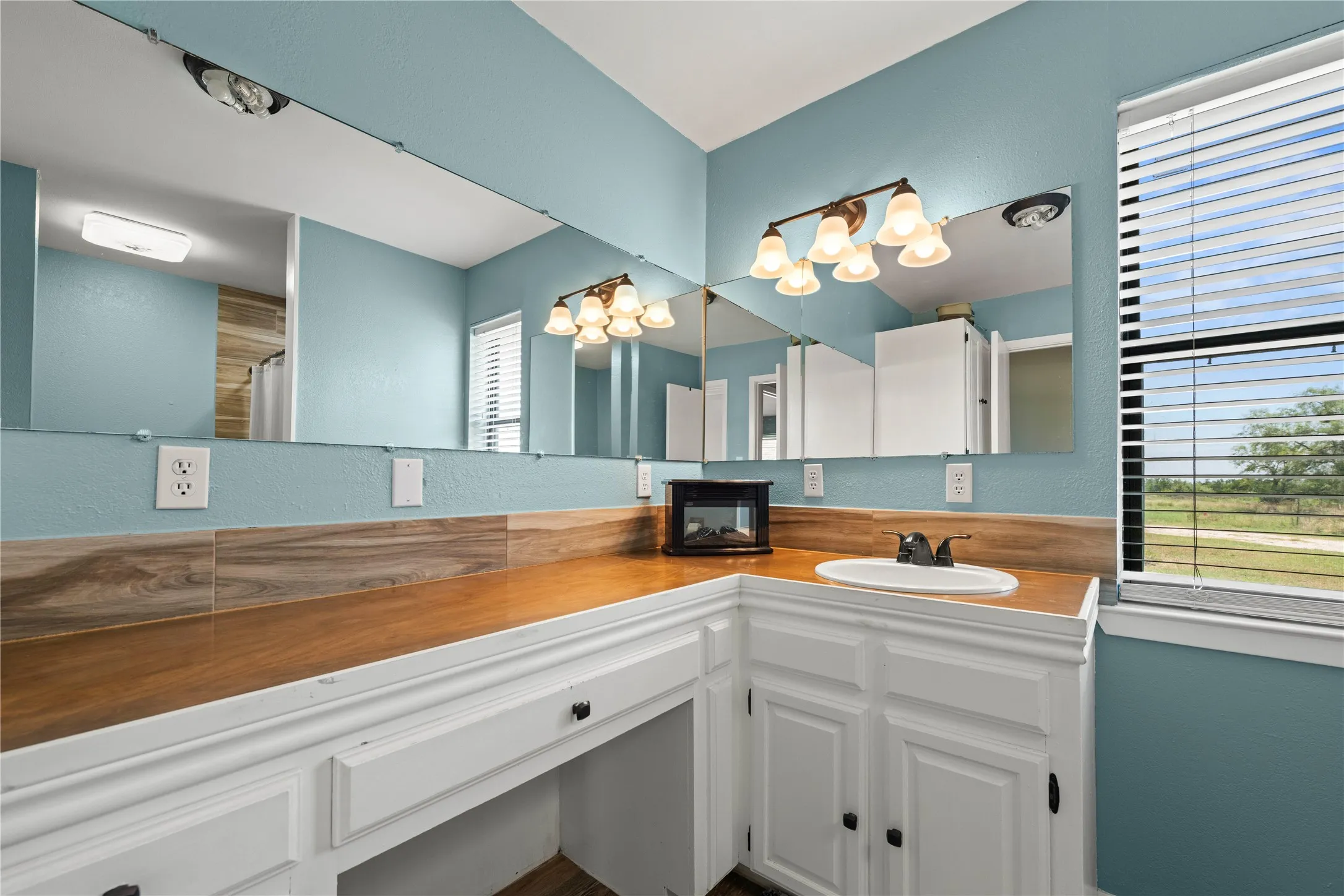 Primary bathroom offering a spacious vanity, soft coastal blue walls, and plenty of natural light overlooking the property