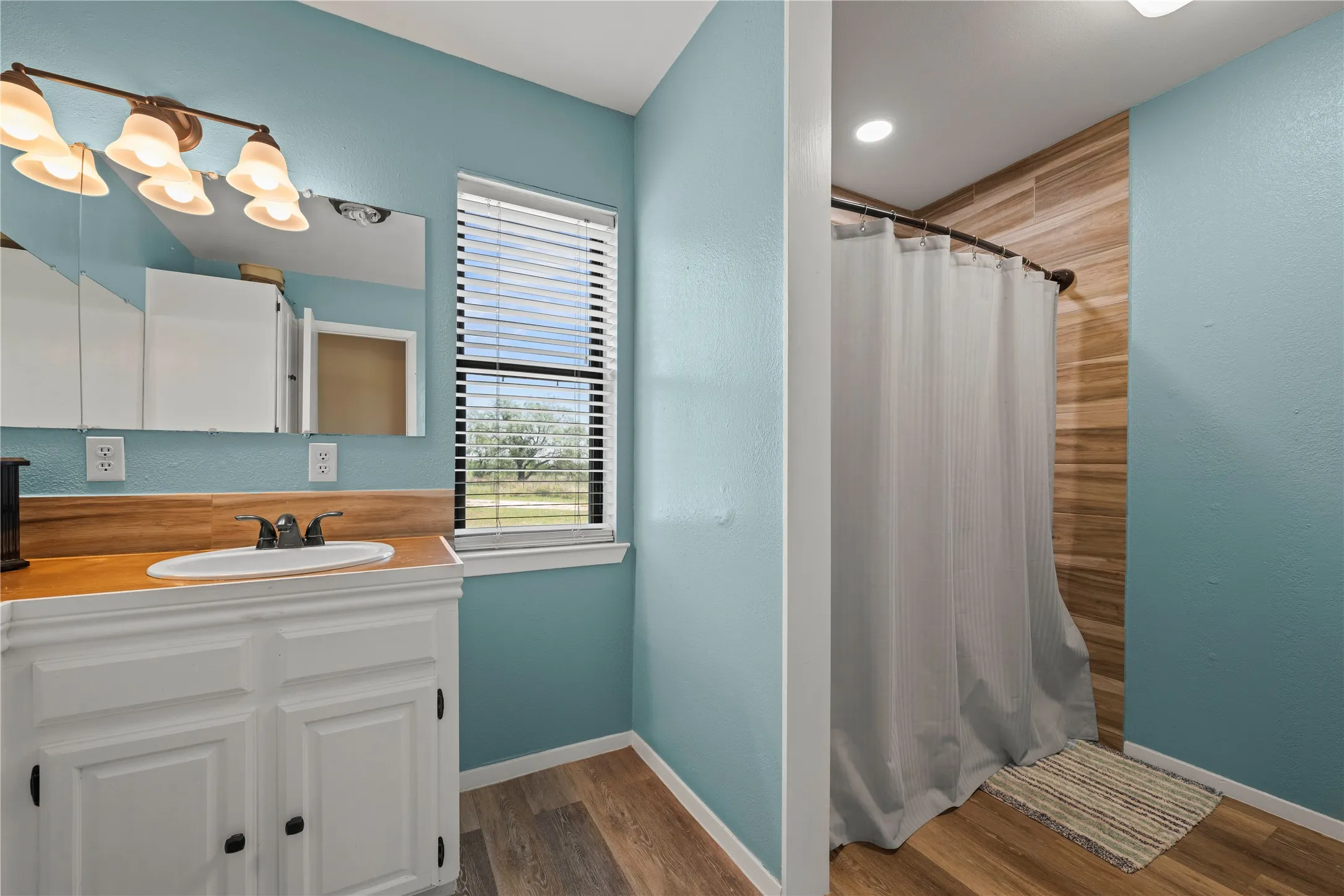 Ensuite bathroom continues with a second vanity area and a walk in shower finished with warm laminate wood flooring