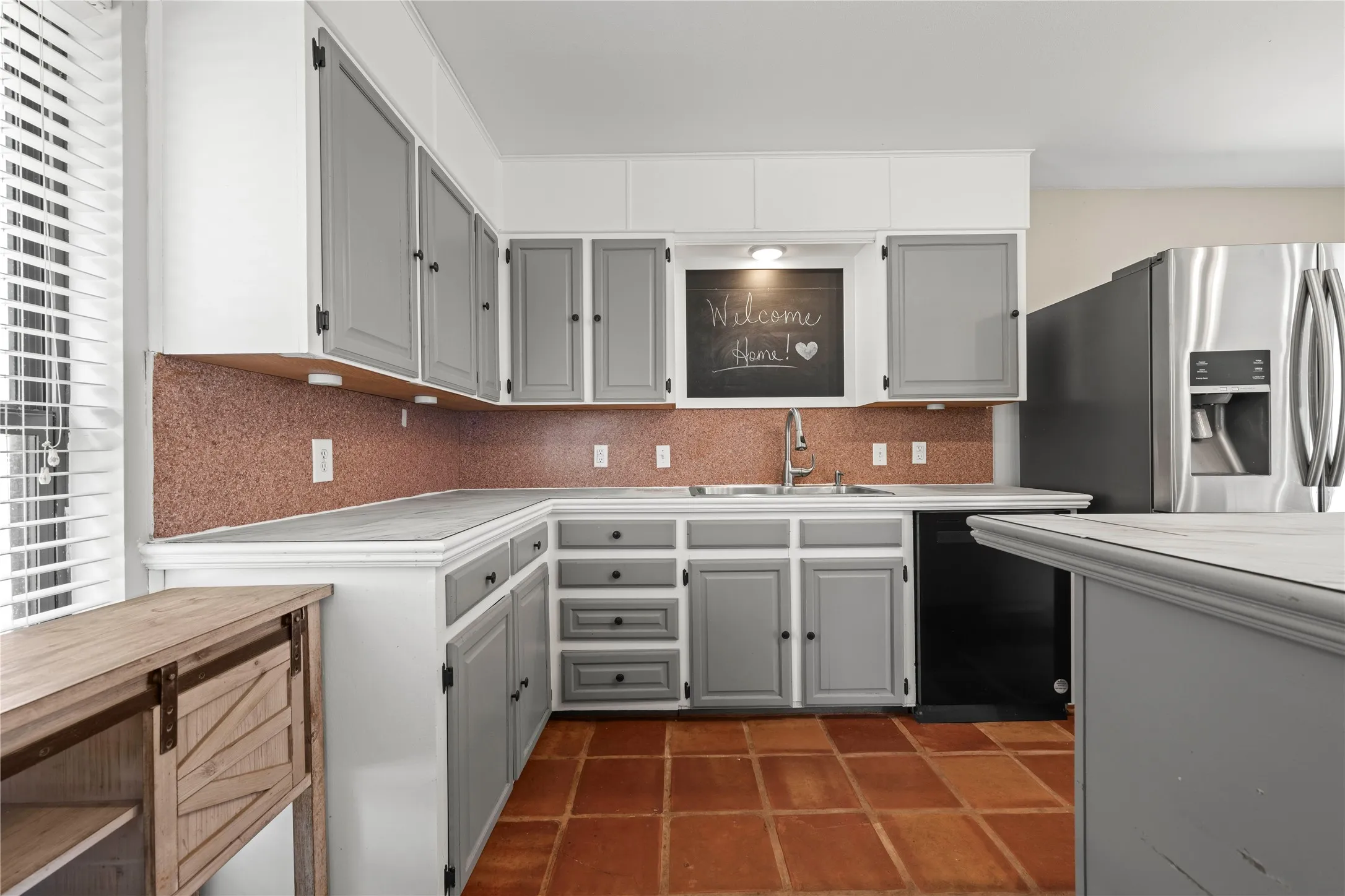 Charming kitchen corner with gray cabinetry, stainless refrigerator, and a sweet Welcome Home touch that sets the tone for this property.
