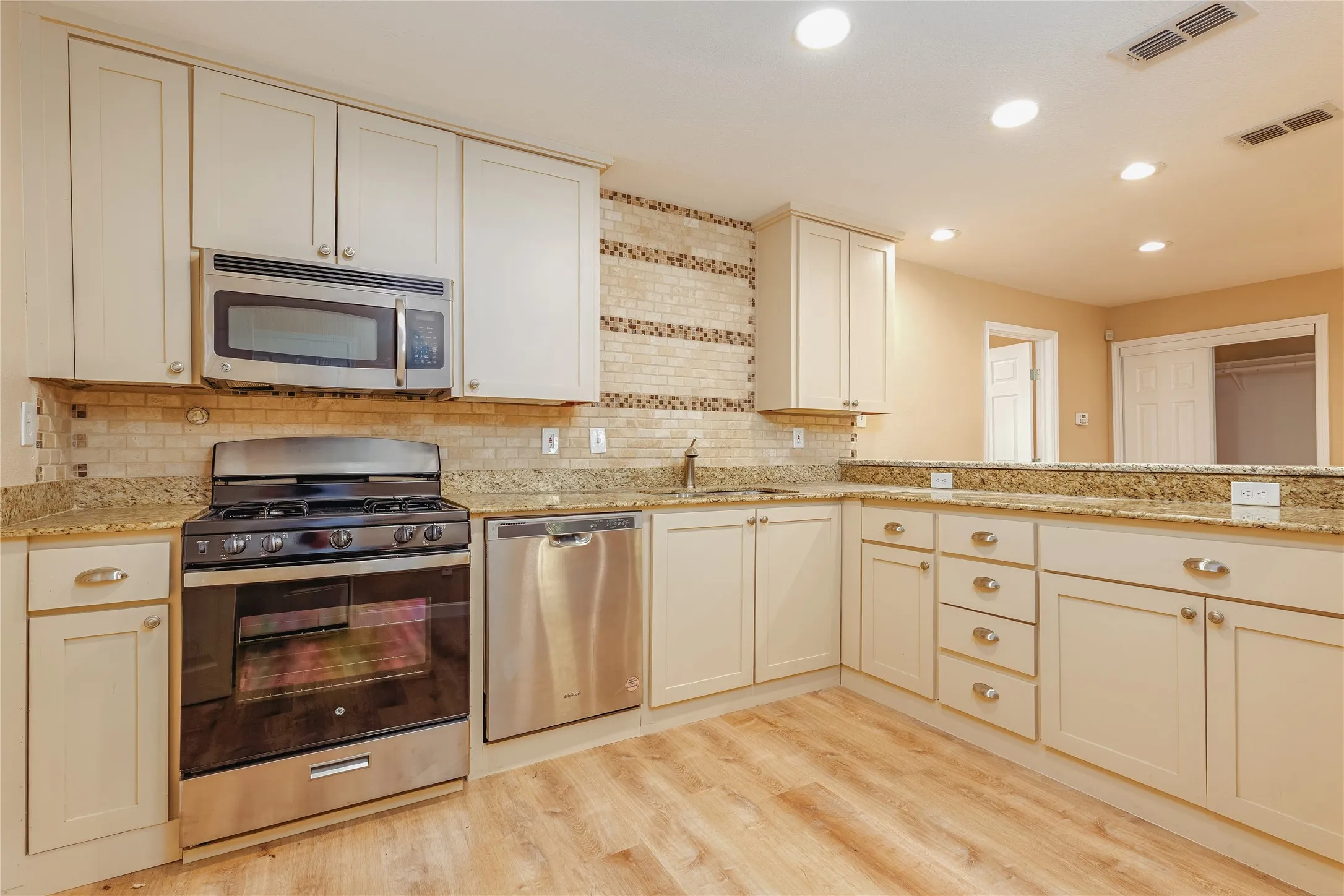 Kitchen featuring light LVP flooring, light cabinetry, stainless steel appliances, and a tiled backsplash