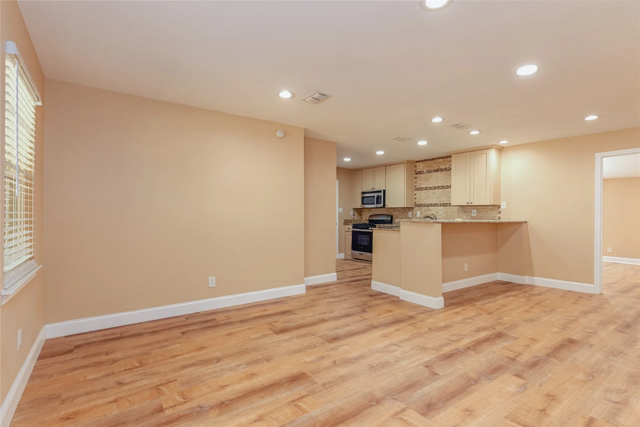 LVP flooring throughout, recessed lighting, and kitchen with stainless steel appliances, light cabinetry, and mosaic tile backsplash