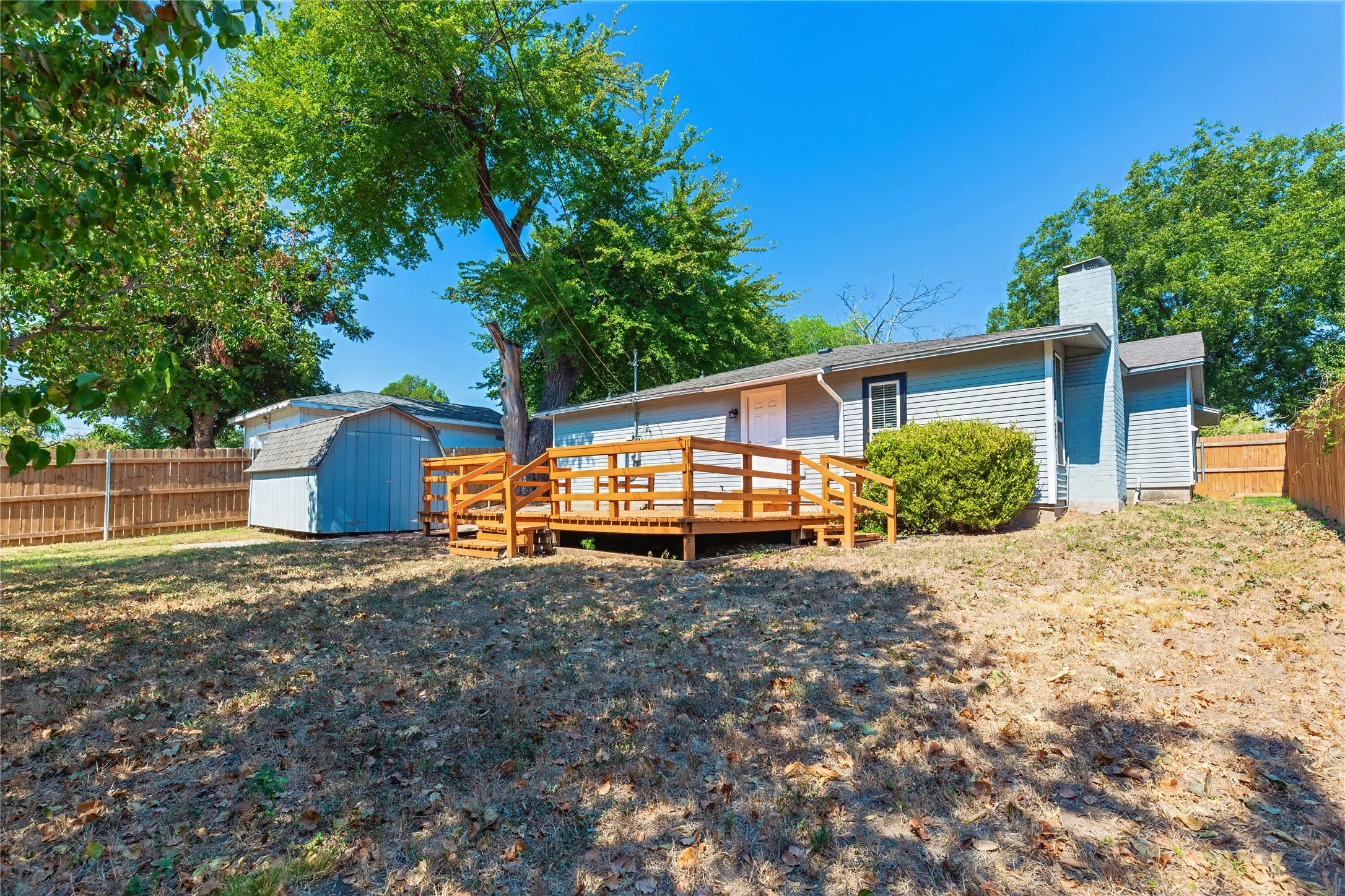 Rear exterior with wood decking, wood fence, and a detached shed