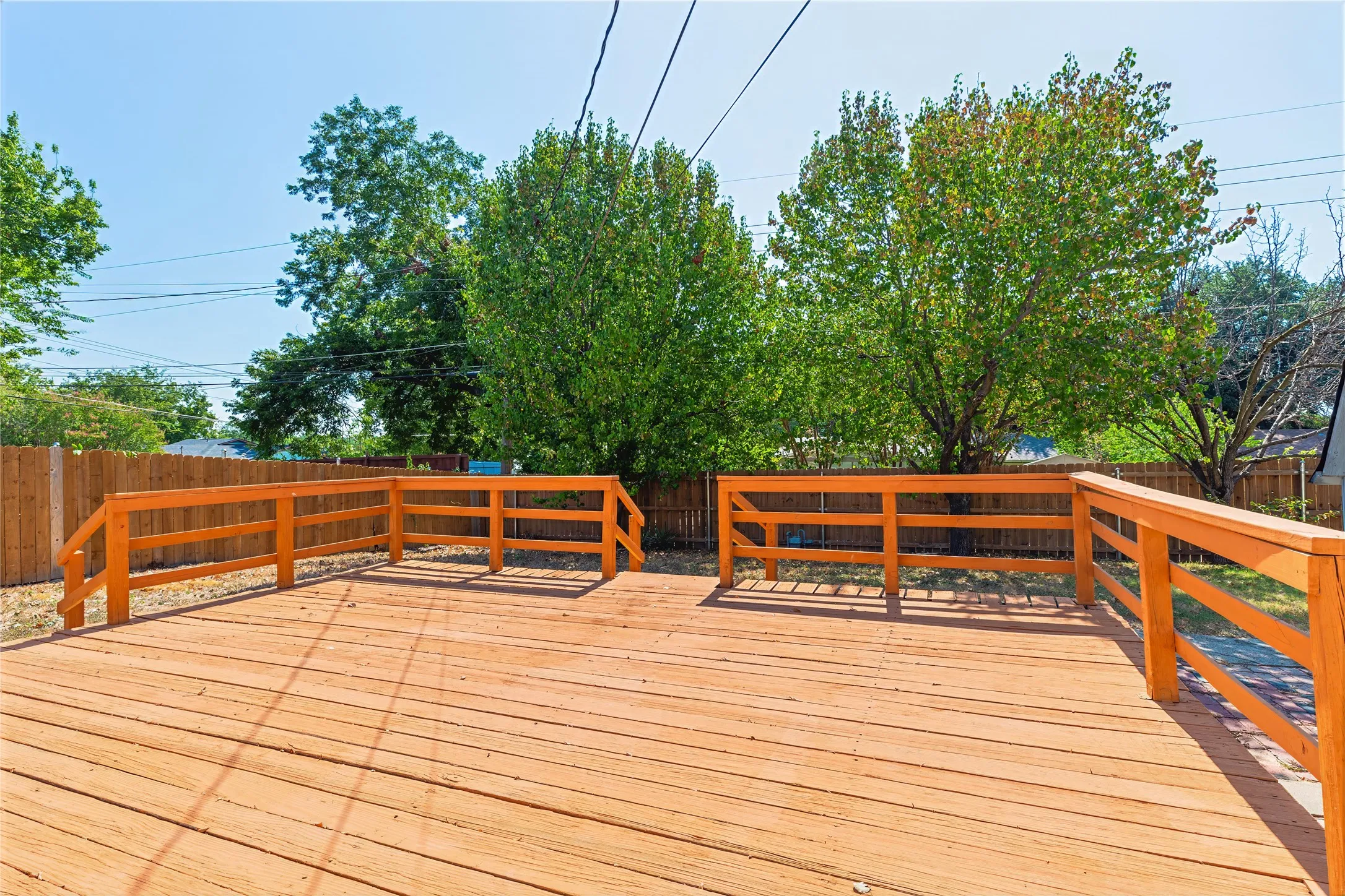 Expansive wooden deck with coordinating railings, bordered by a privacy fence and mature trees