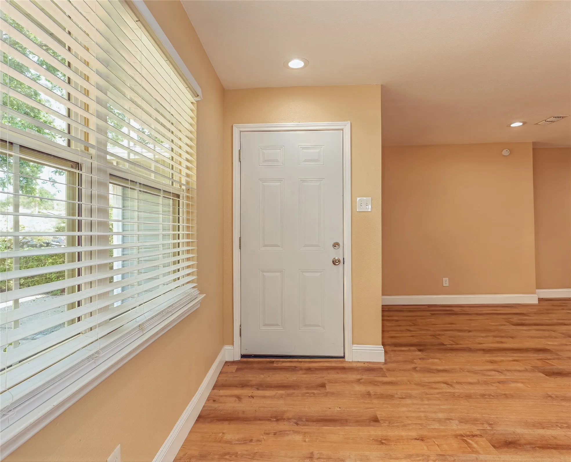 LVP flooring, recessed lighting, window with horizontal blinds, and a paneled entry door
