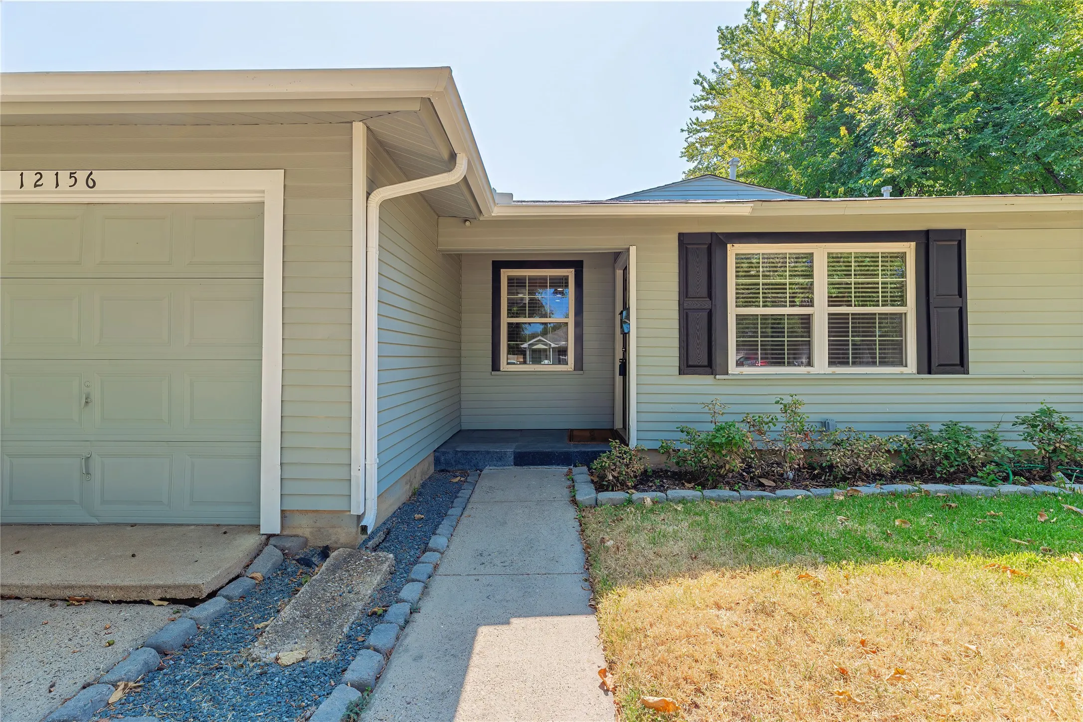 Light-colored grey siding exterior with dark shutters, attached garage, and a concrete pathway