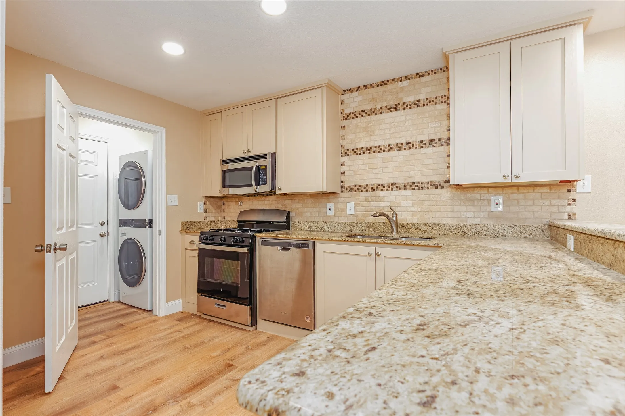 Kitchen featuring granite countertops, stainless steel appliances, LVP flooring, and a tiled backsplash