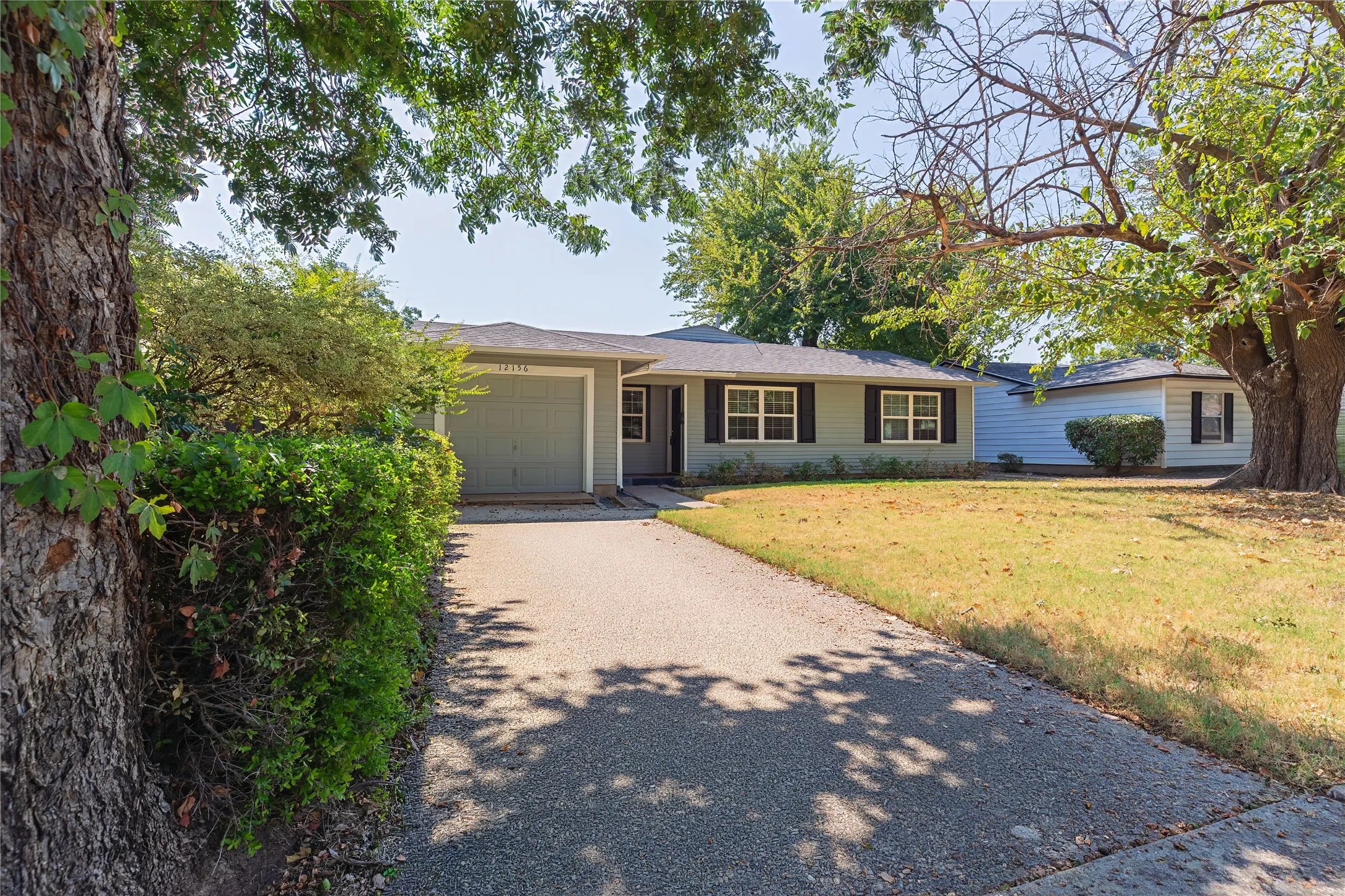 Ranch-style exterior with light green siding, black window shutters, a front-facing garage, and a paved driveway