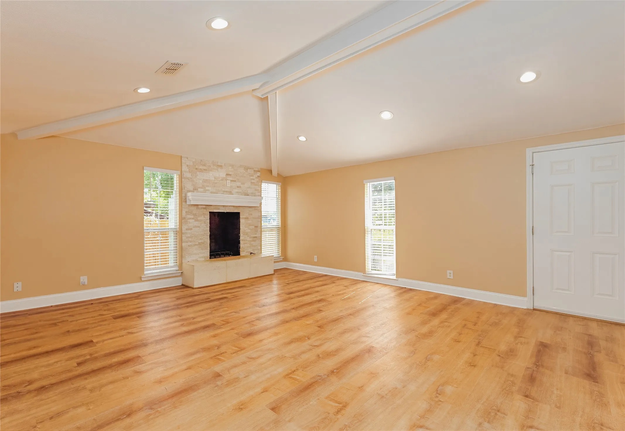 Vaulted ceiling with exposed beams, recessed lighting, LVP flooring, stacked stone fireplace