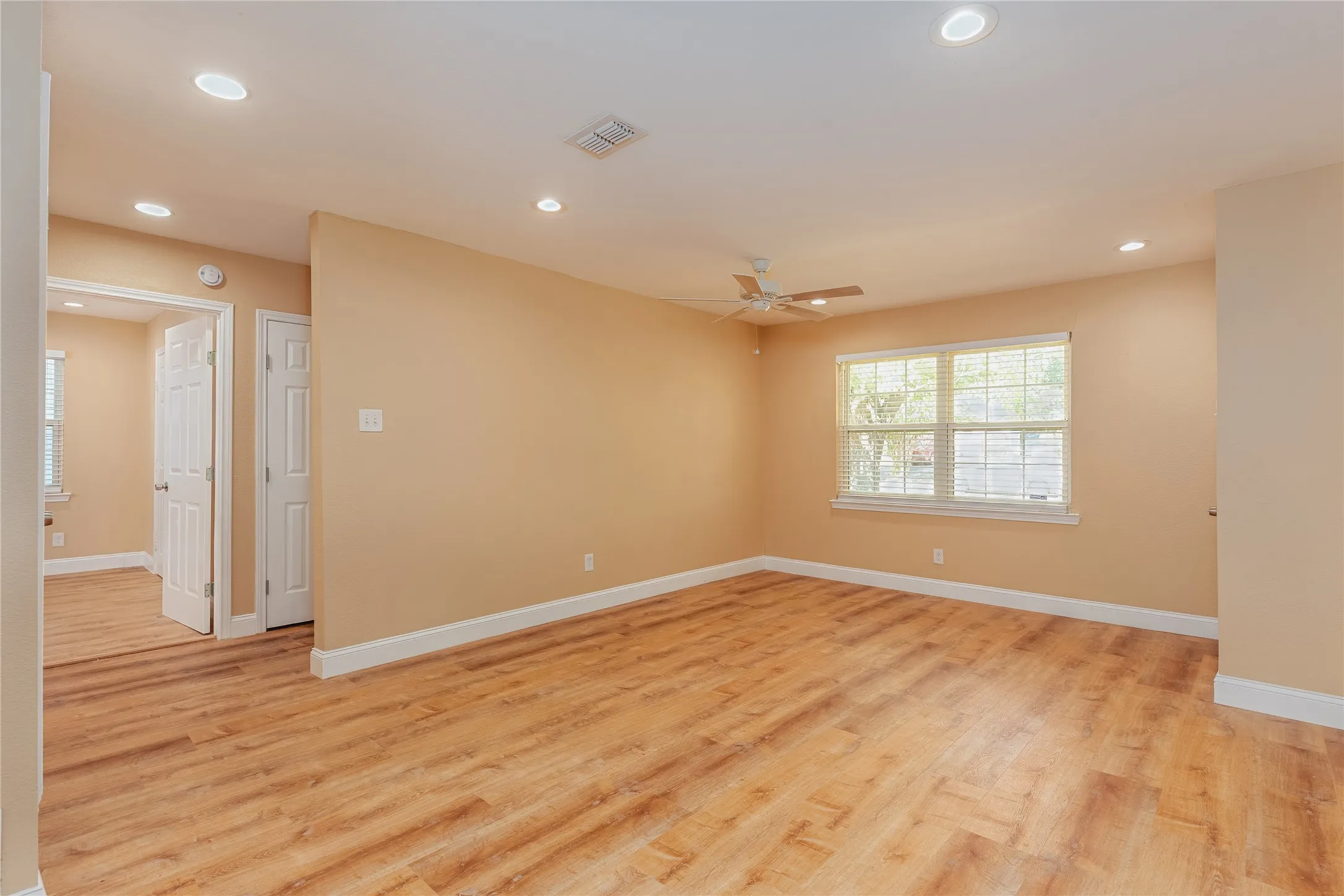 Spacious room featuring LVP flooring, recessed lighting, a ceiling fan, and a large window with blinds
