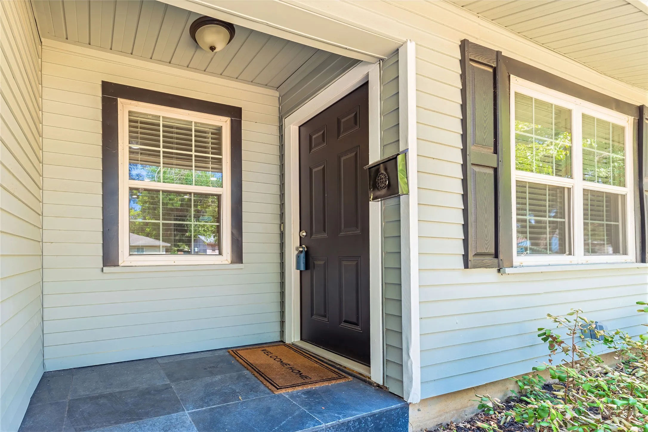 Front entry featuring light grey siding, dark paneled door, black exterior shutters, and a tiled porch