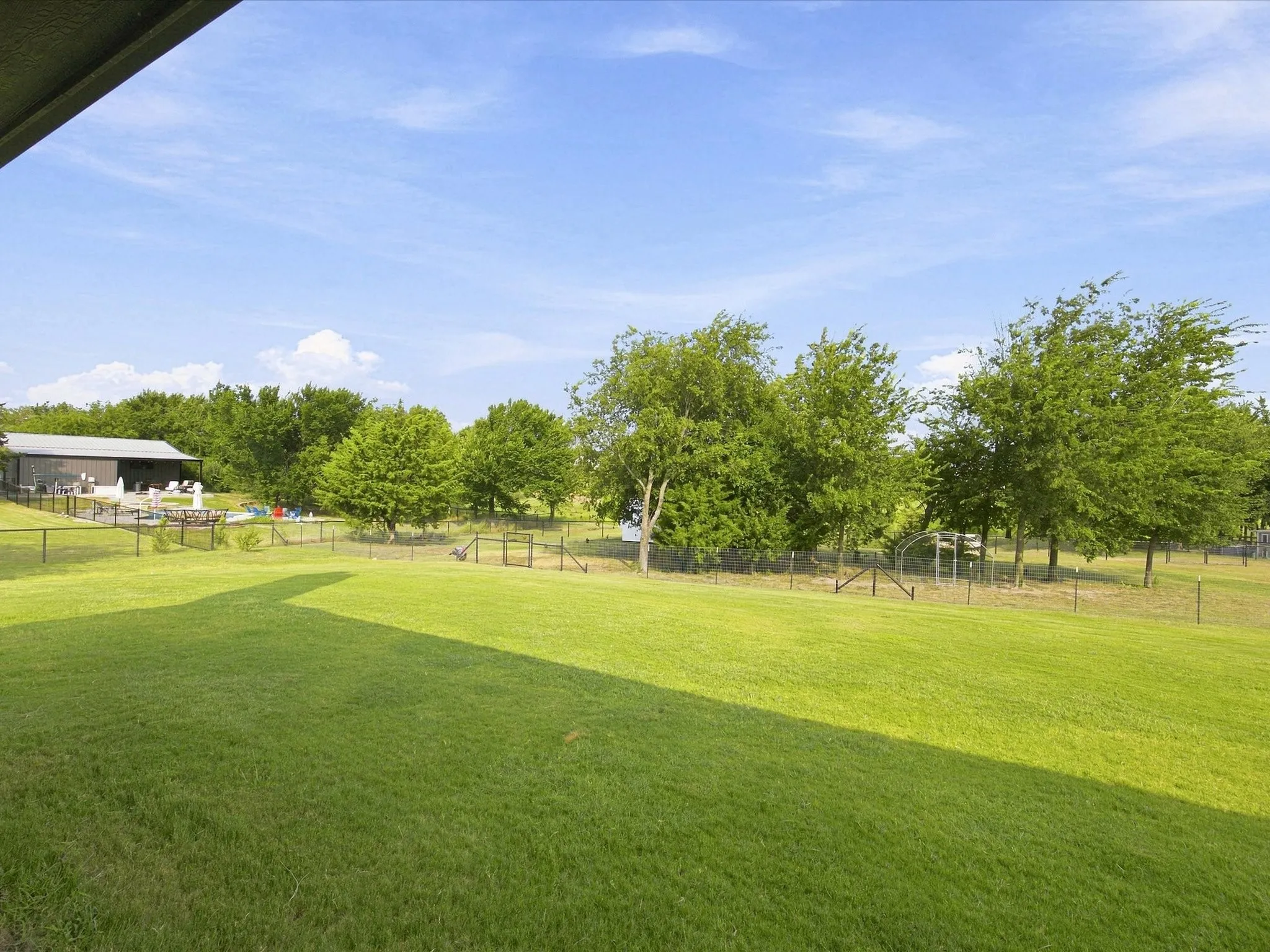 Expansive grassy area with mature trees and perimeter fencing