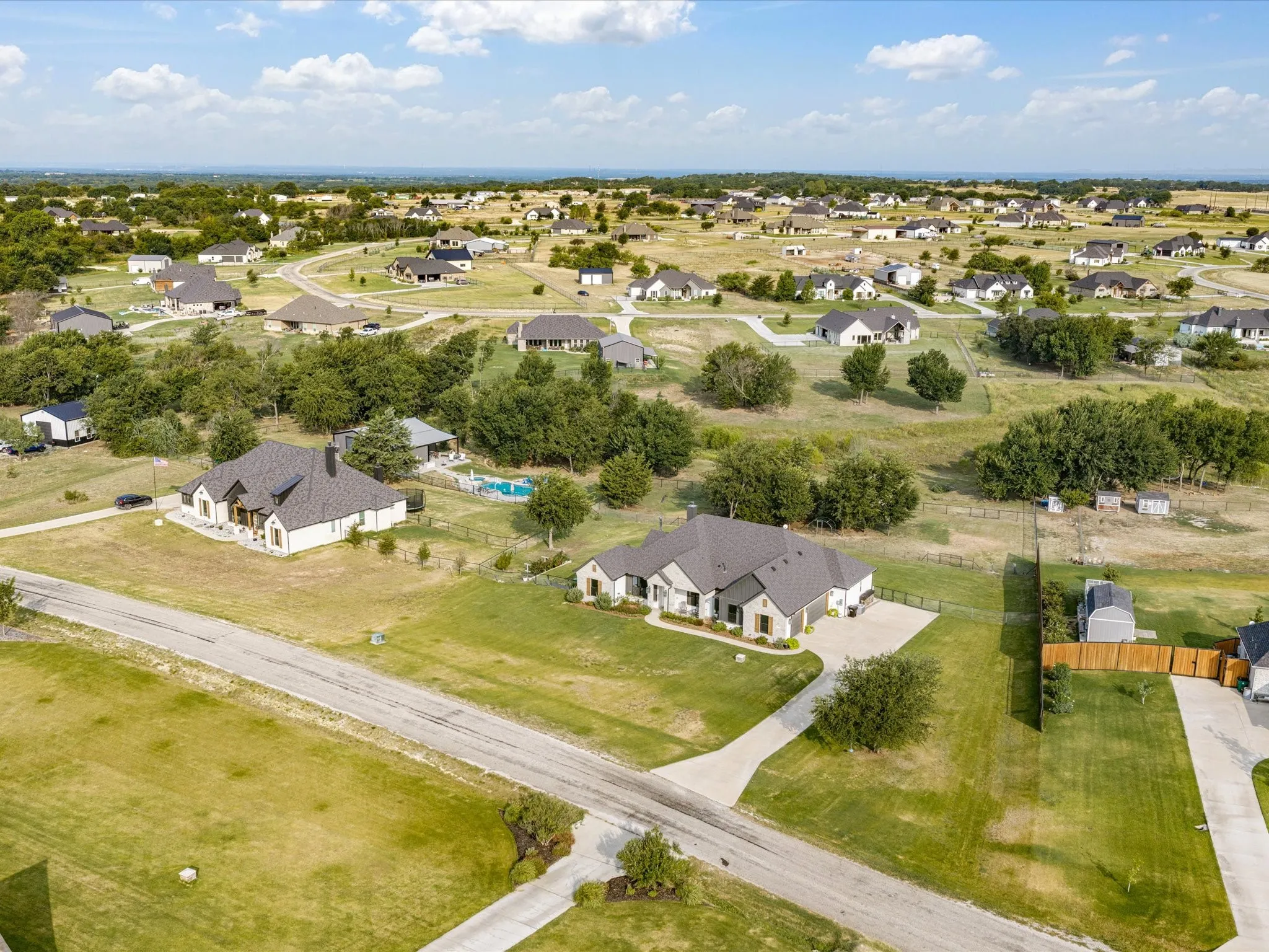 Expansive residential property featuring a modern ranch-style home with dark architectural roofing, situated on substantial acreage with mature landscaping