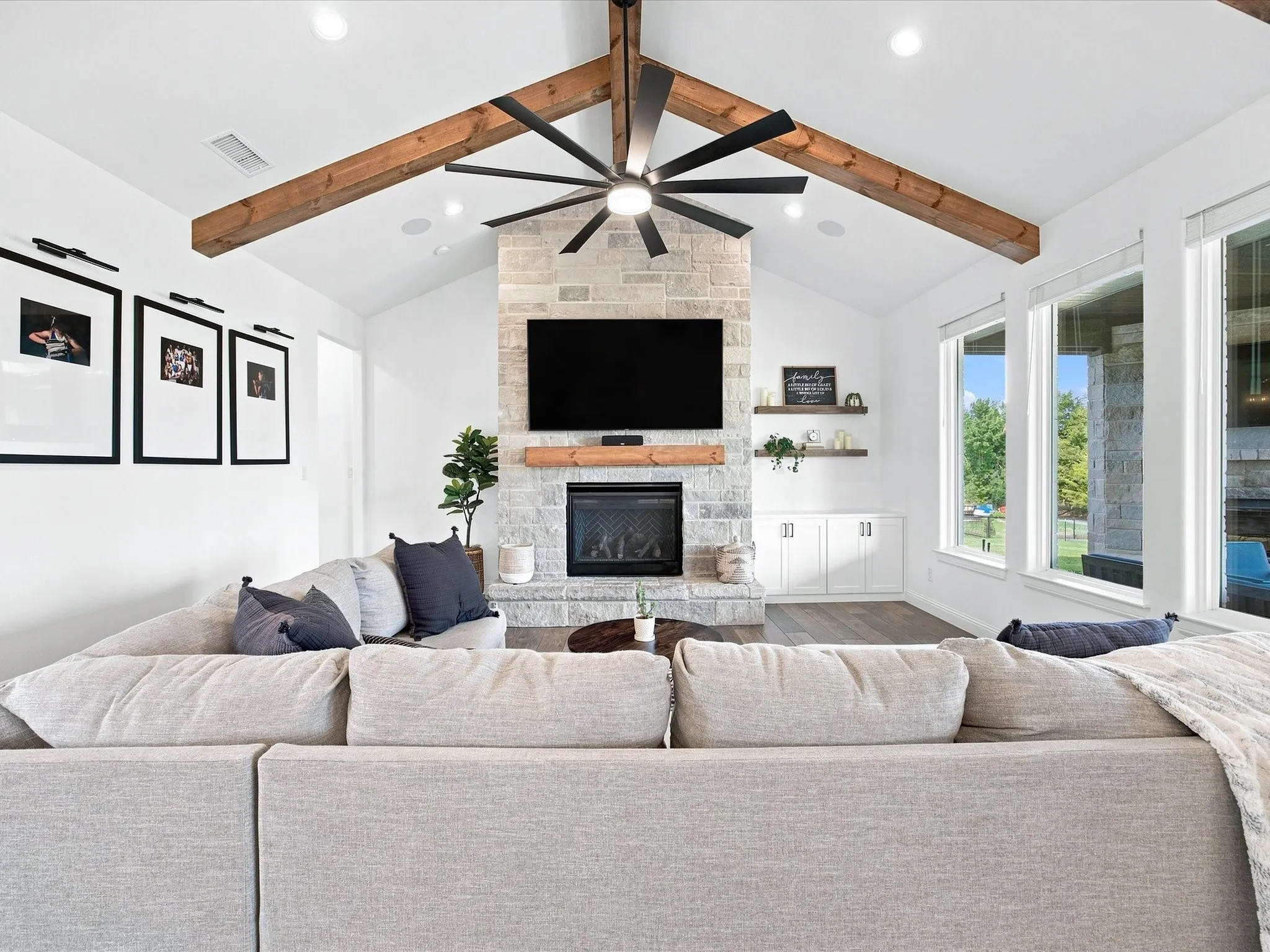 Vaulted ceiling with exposed wood beams, stone-faced fireplace, wood-finish flooring, built-in cabinetry, and large windows