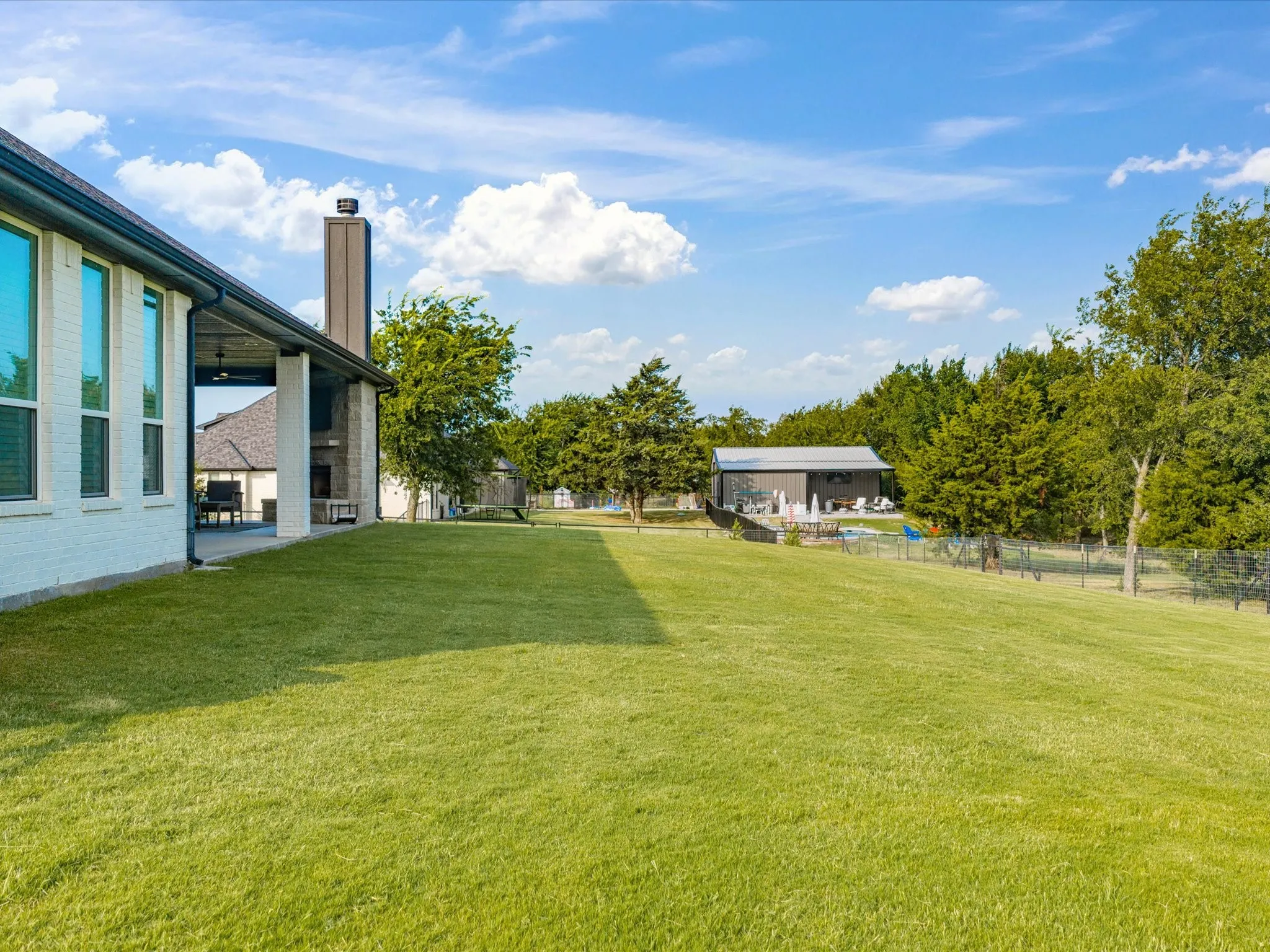 Expansive green lawn with a covered patio, a detached structure, and mature trees