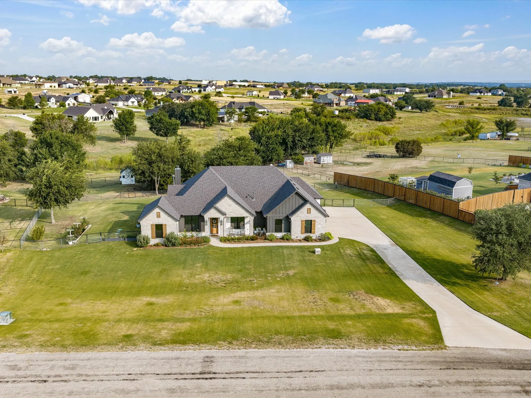 Striking Contemporary residence set on expansive grounds featuring a cream and dark exterior with clean architectural lines, mature landscaping throughout the property, a long paved driveway approach, and open acreage with established trees and pastoral surroundings