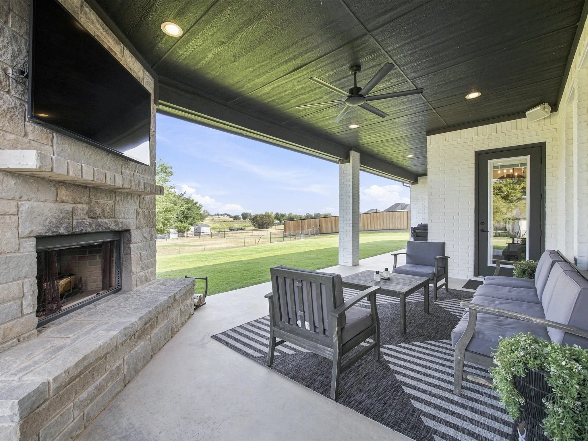 Covered patio with stone fireplace, ceiling fan, and recessed lighting overlooking expansive manicured lawn