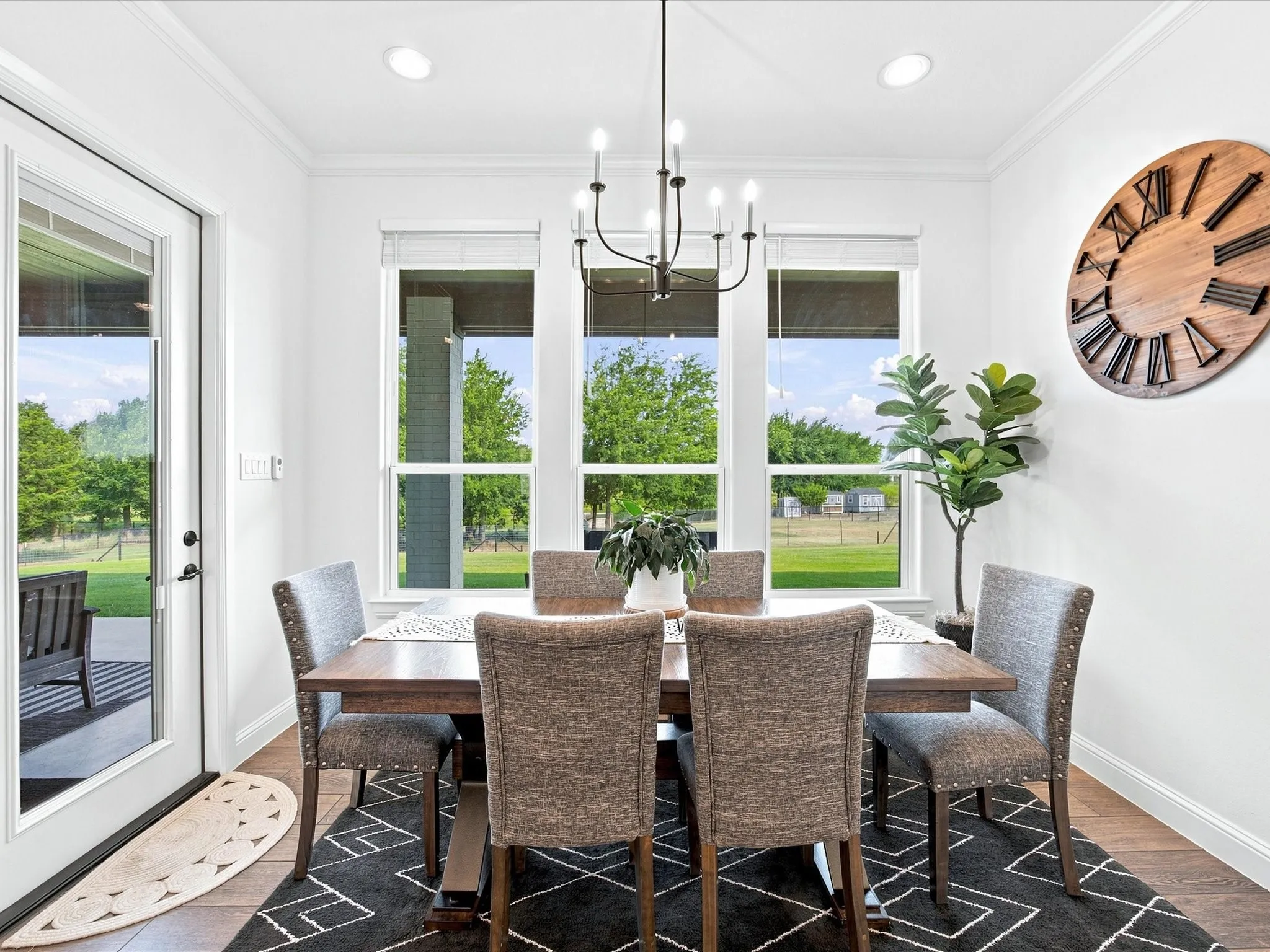 Bright dining room anchored by a wood-finish table and upholstered chairs, illuminated by a contemporary chandelier
