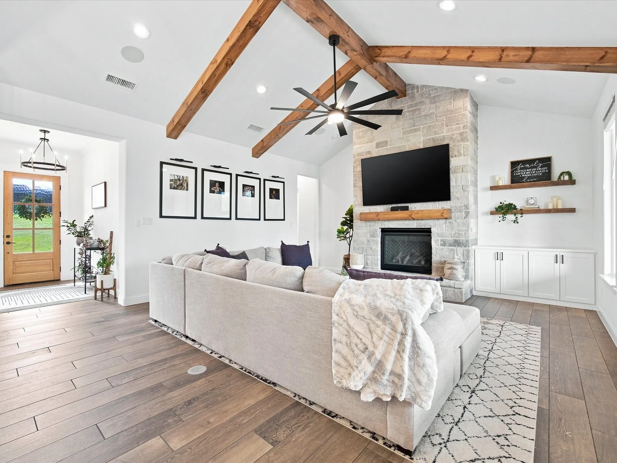 Vaulted ceiling with exposed wood beams, stone-faced fireplace with wood mantel, wood-finish flooring, built-in cabinetry, and a wood-panel entry door
