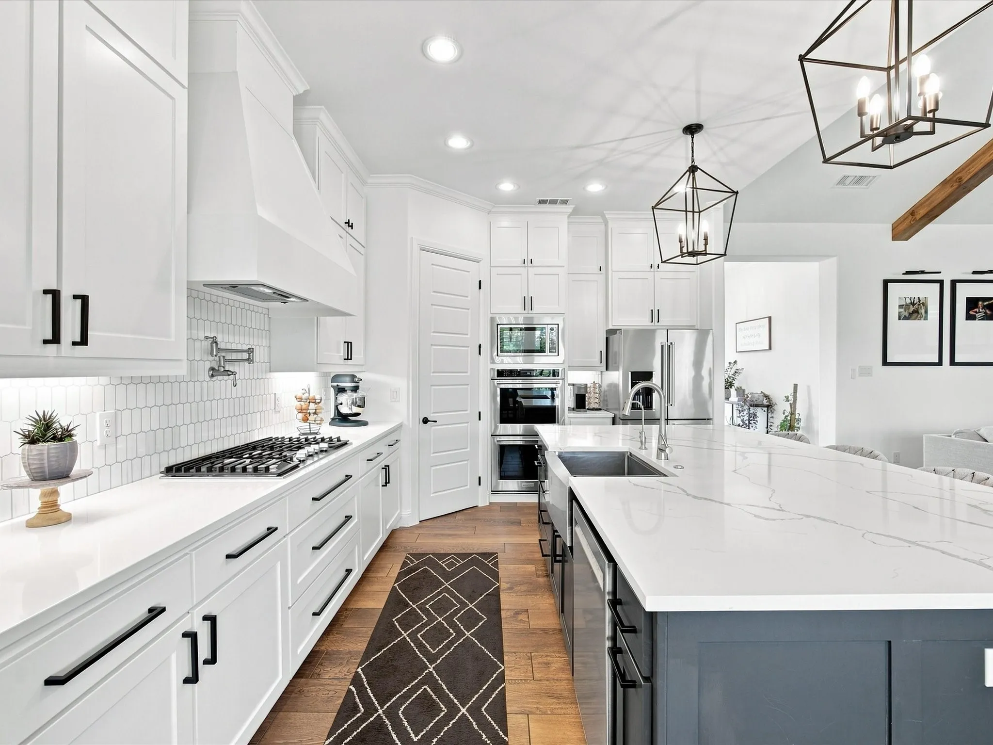 Gourmet kitchen with white cabinetry, stainless steel appliances, a pot filler, and a large central island with an undermount sink