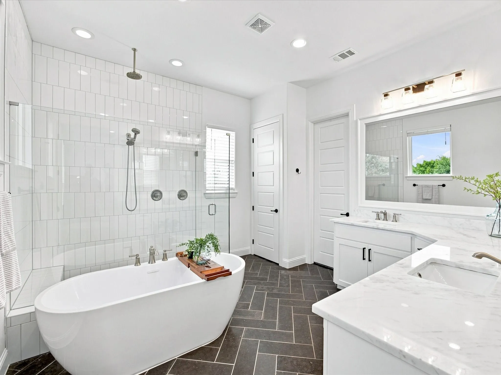 Freestanding soaking tub, walk-in shower with vertical tile surround, dual vanity with undermount sinks, and herringbone tile flooring