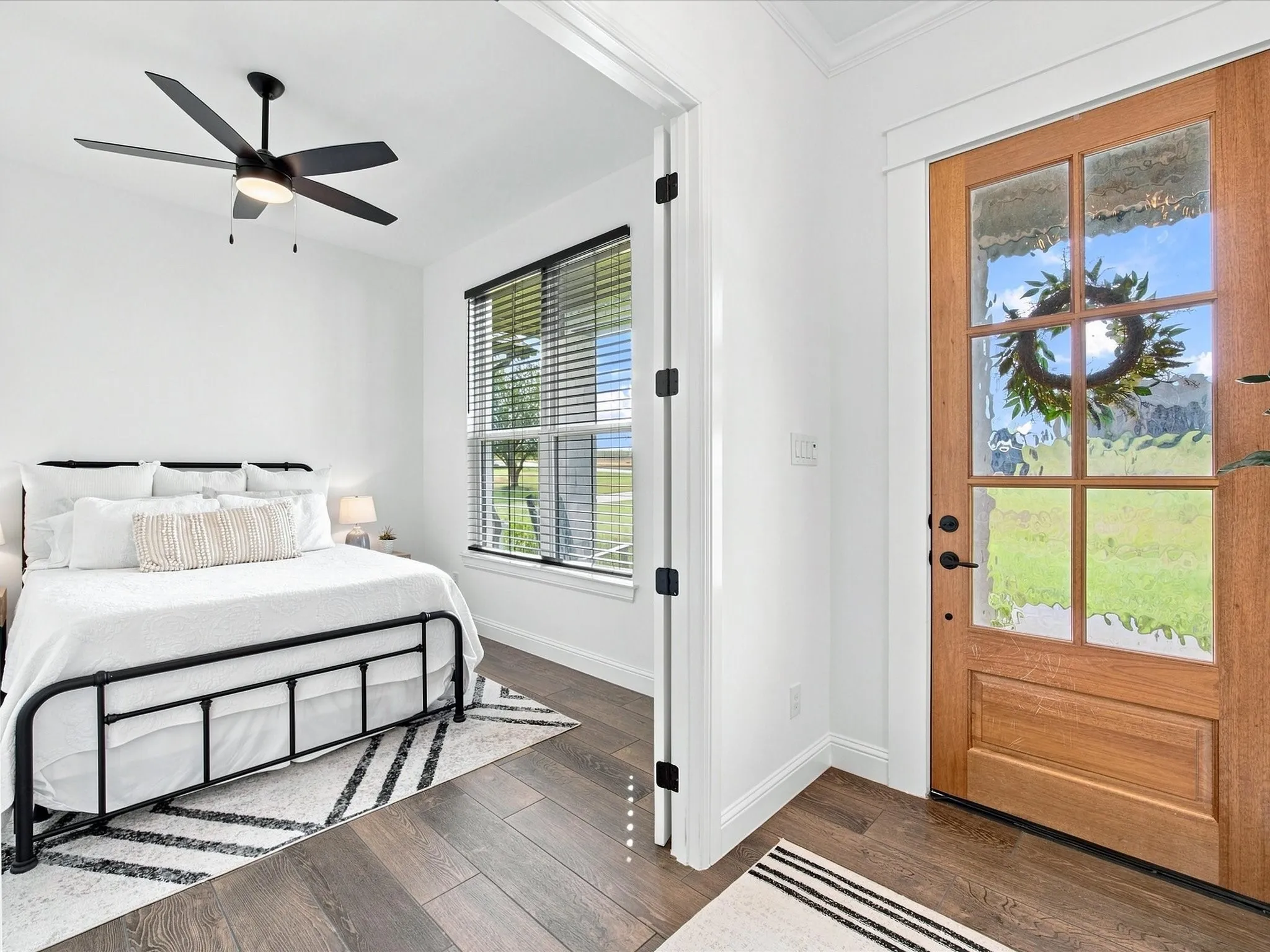 Wood-finish flooring throughout, framed window with blinds, solid wood door with glass panels, recessed lighting, and a ceiling fan with integrated lighting