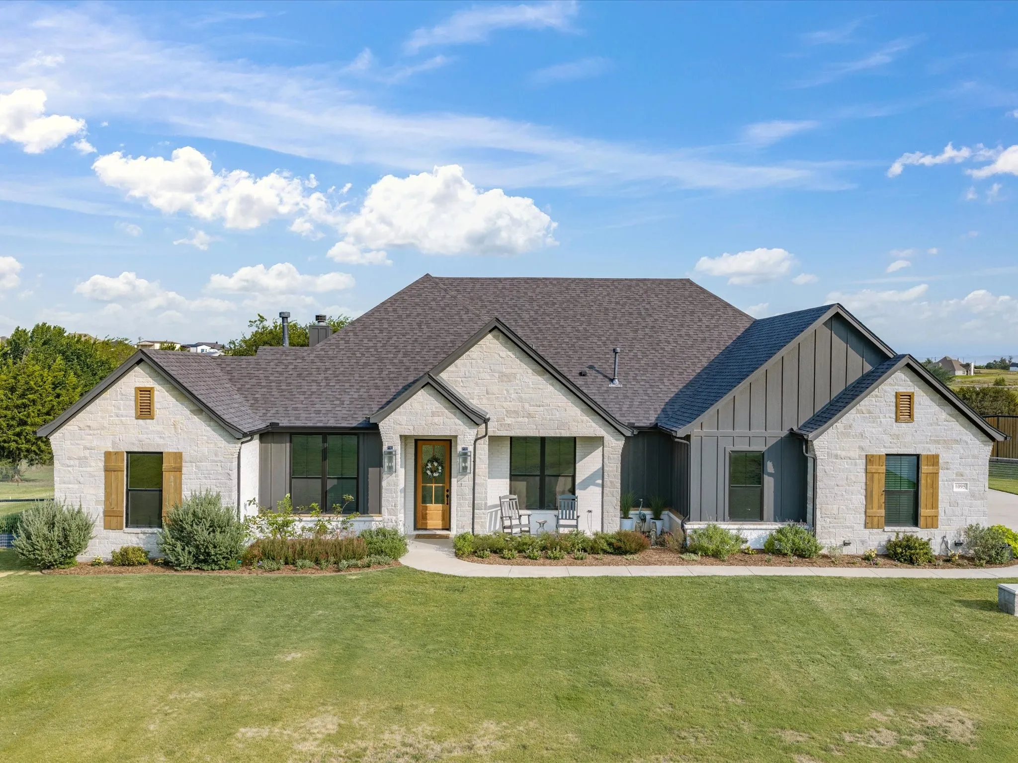 Modern farmhouse residence showcasing a white brick and board-and-batten exterior, multi-gabled roofline with architectural shingles, and symmetrical facade with black-trimmed windows and gold-finished hardware