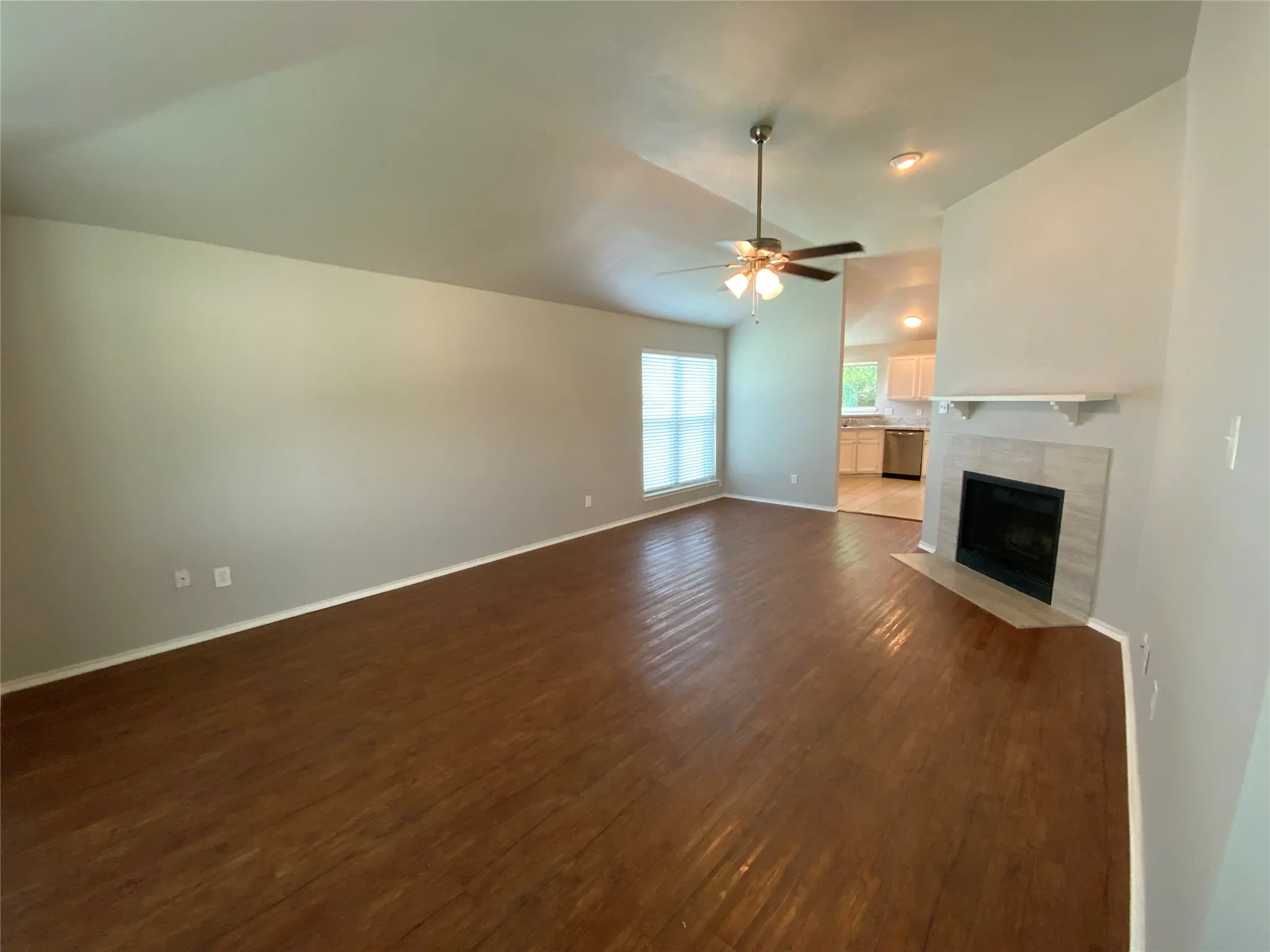 Spacious living area featuring wood-finish flooring, a vaulted ceiling, and a fireplace with a tile surround and mantel