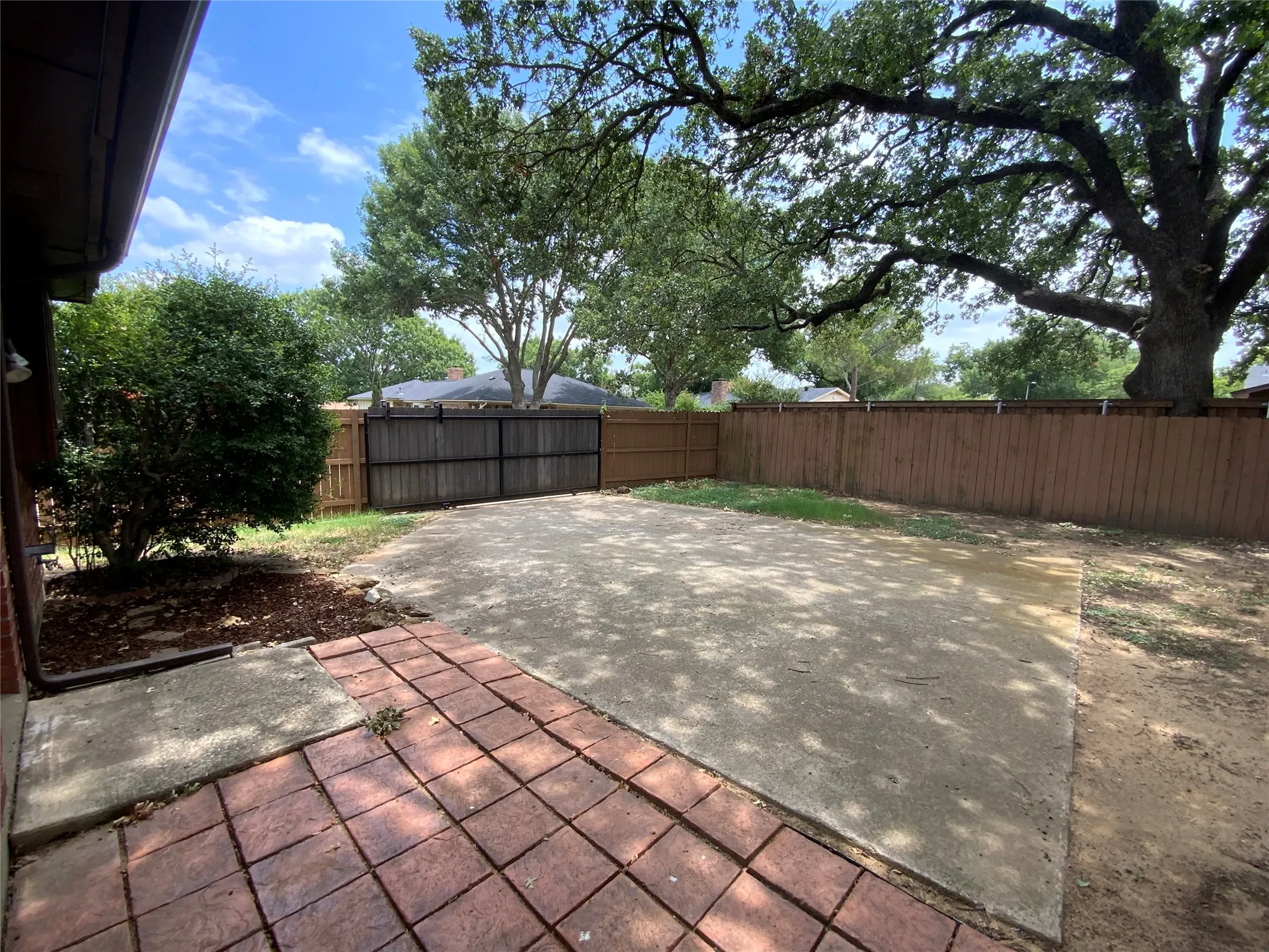 Expansive outdoor space featuring a large concrete patio, a stamped brick patio area, mature trees, and a wooden privacy fence