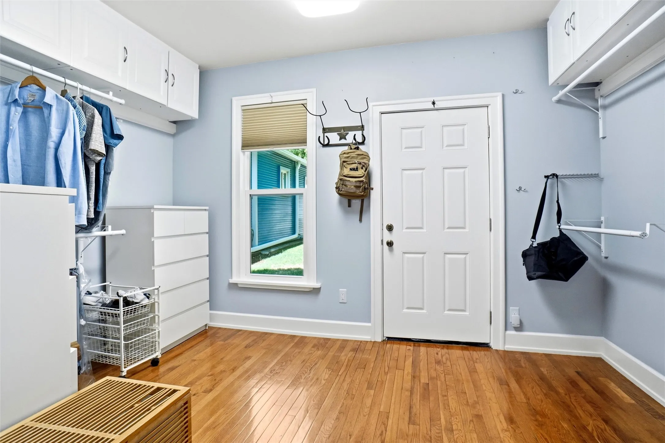 Hardwood flooring throughout this versatile space featuring white baseboards, a paneled door, and a single window with blinds