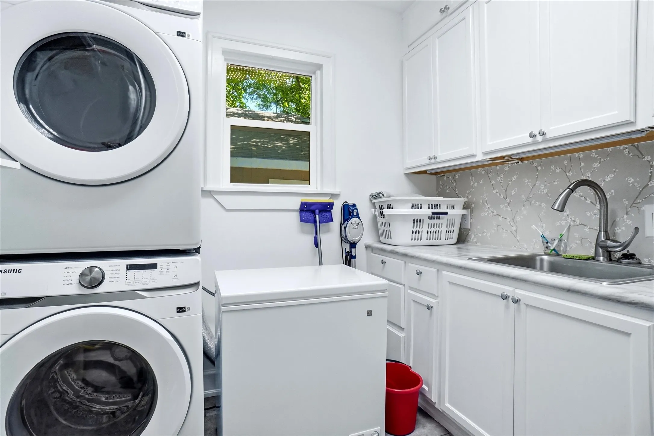 Dedicated laundry space featuring a window, white cabinetry, a sink with a gooseneck faucet, light-toned countertop, and a decorative backsplash