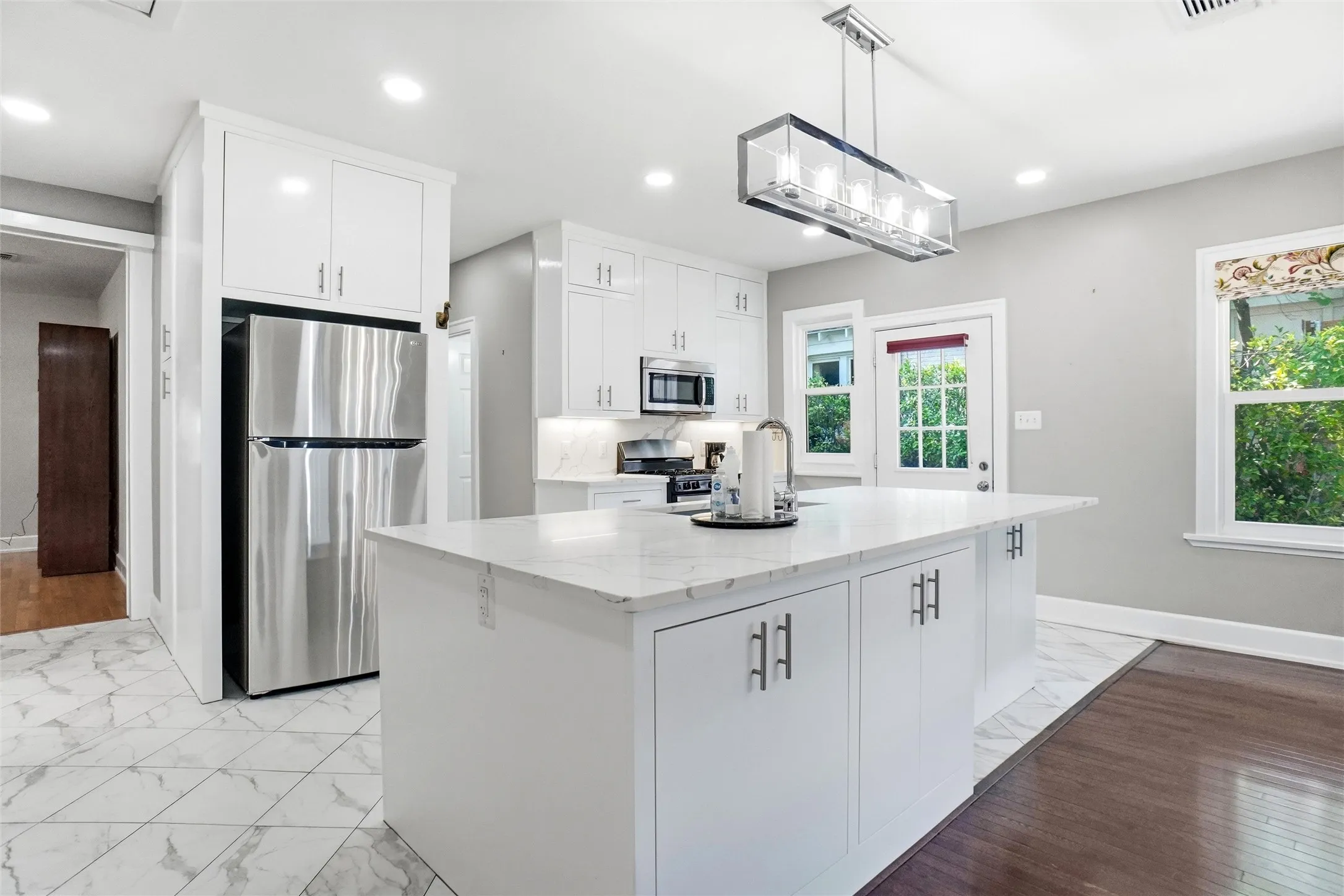 Modern kitchen featuring white cabinetry, a large center island with a quartz-finish countertop, stainless steel appliances, and a contemporary linear chandelier