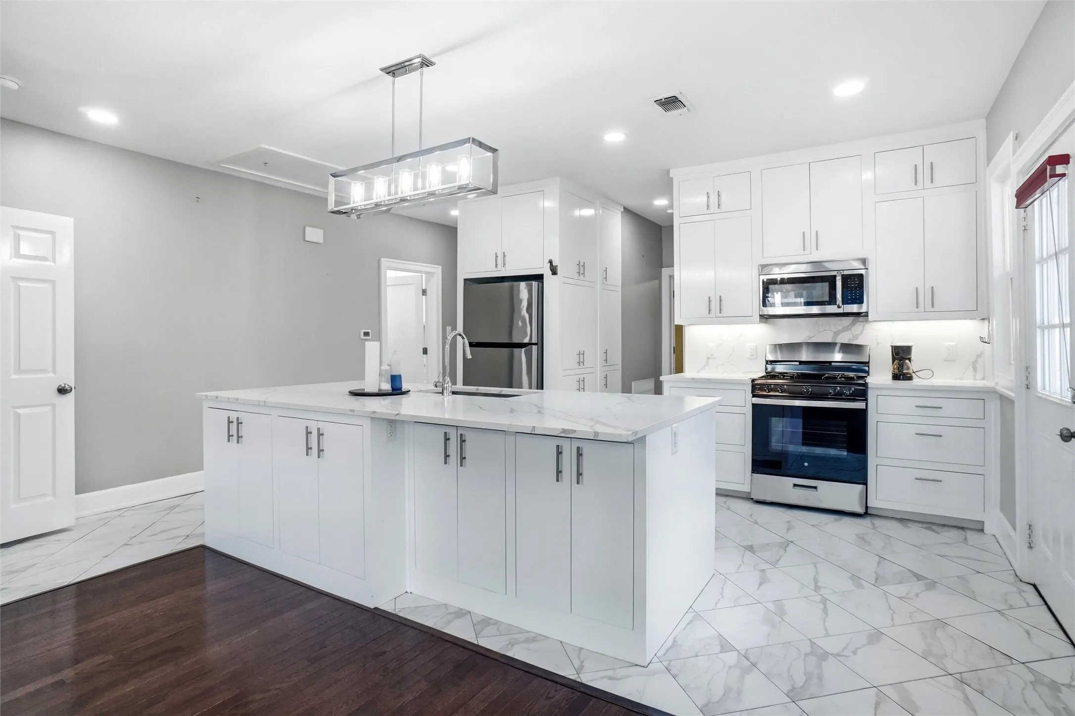 Kitchen featuring white cabinetry, stainless steel appliances, a center island with sink, marble-finish countertops, and patterned tile flooring
