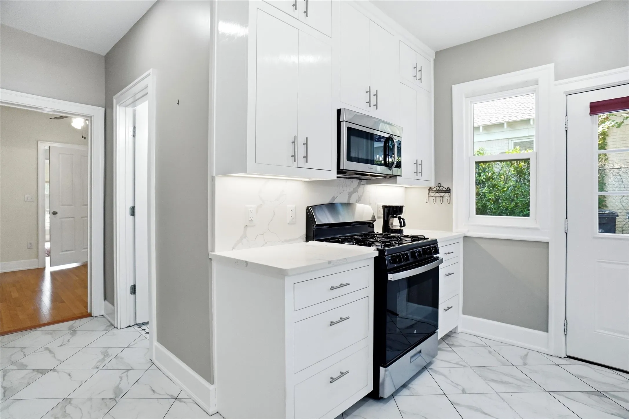 Kitchen featuring bright white cabinetry, stainless steel microwave, gas range, marble-patterned countertops, and tile flooring