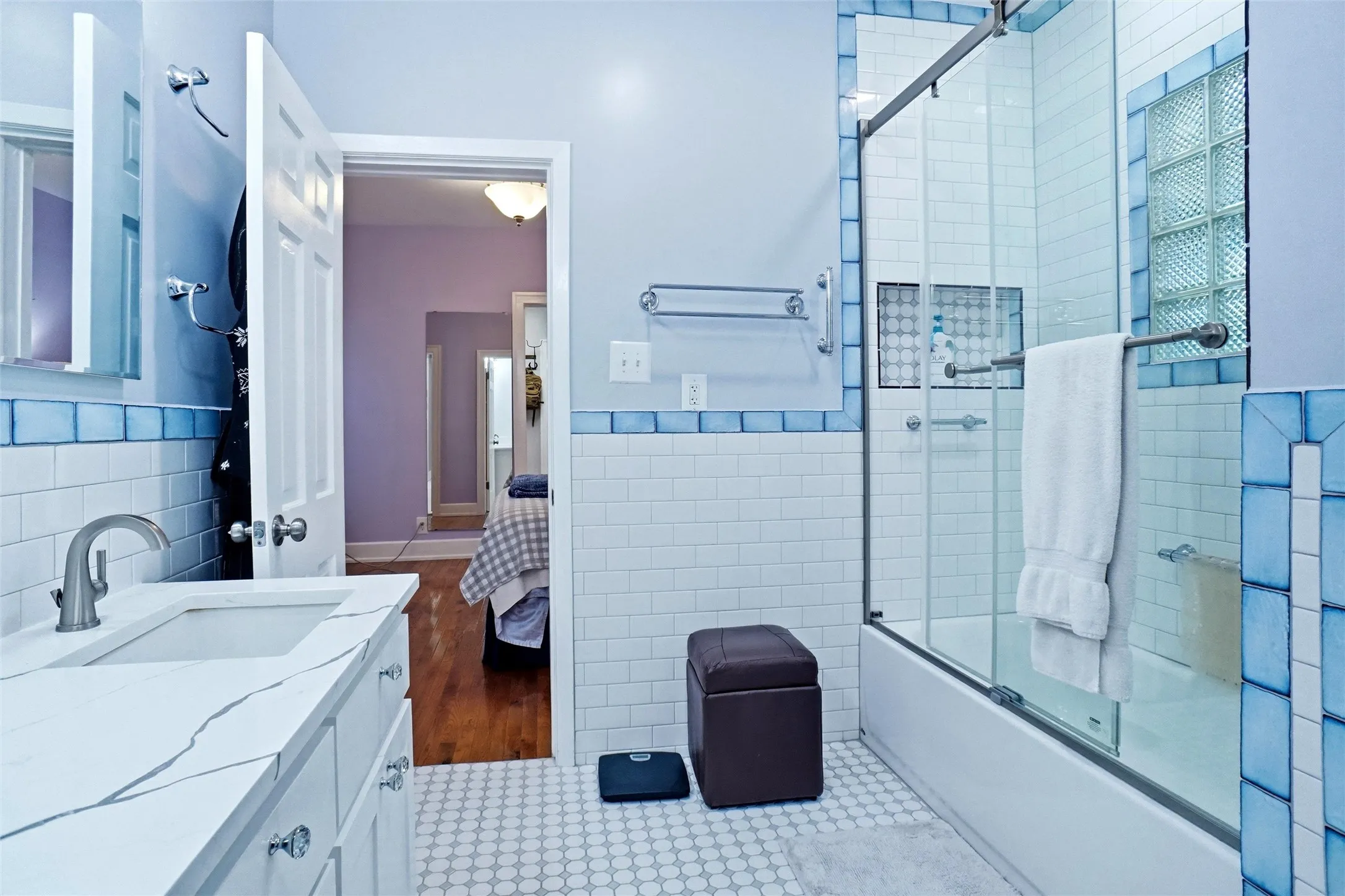 Bathroom featuring a white subway tile surround with blue accent tiles, a single vanity with a white countertop and undermount sink, and a combination tub and shower with a glass enclosure