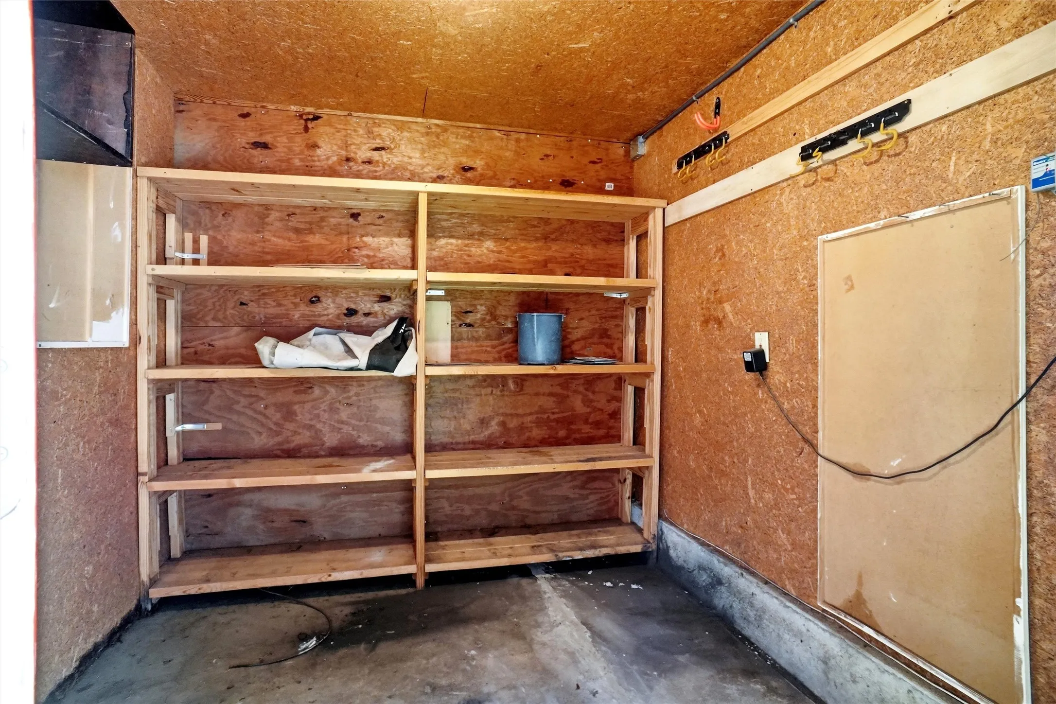 Utility space featuring integrated wood shelving, oriented strand board walls, and a concrete floor