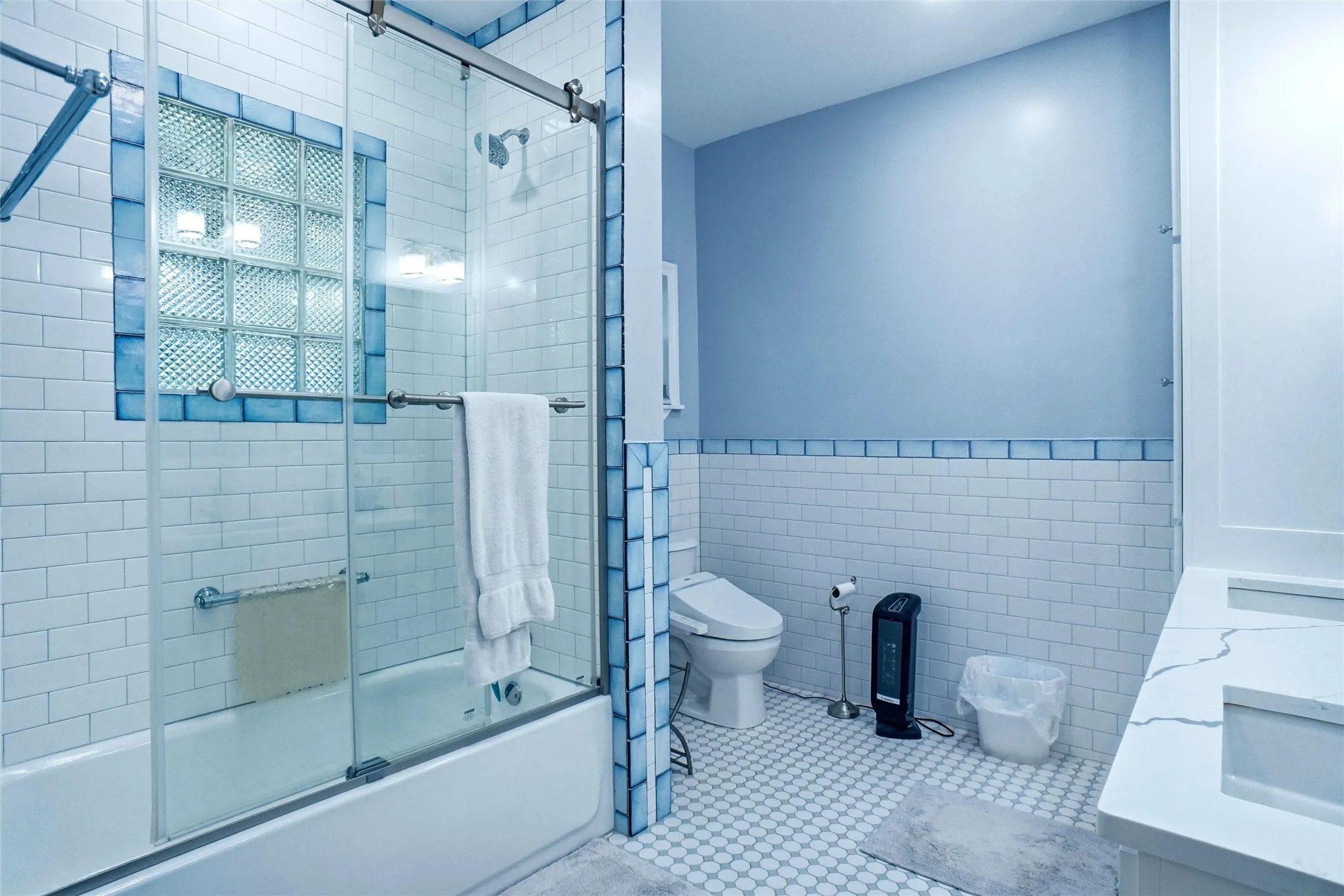 Bathroom featuring a tiled tub-shower combination with glass enclosure, glass block window, and blue accent tiles