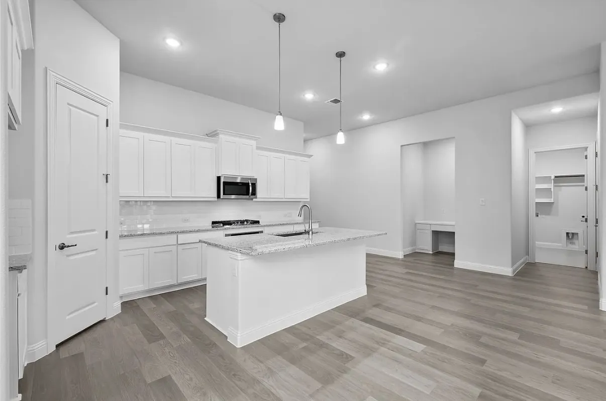 Spacious kitchen featuring white cabinetry, light-toned granite countertops, a stainless steel microwave, and a central island with a sink and pendant lighting