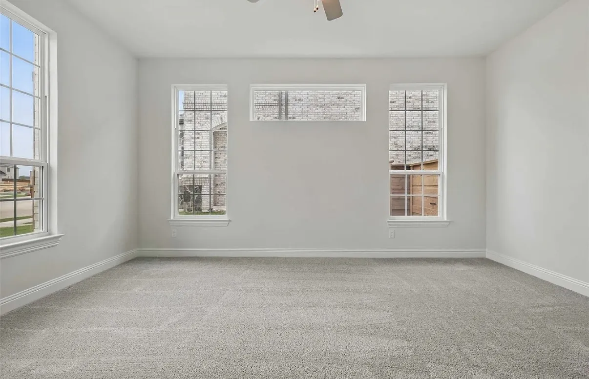 Spacious interior room featuring light gray carpeting, multiple windows with grids, white trim, and a ceiling fan fixture