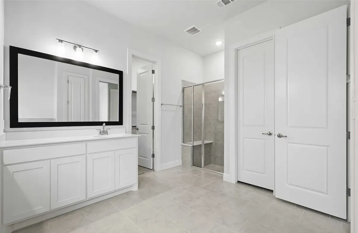 Spacious bathroom featuring a single vanity with storage cabinetry, a framed mirror, and a walk-in shower with a built-in bench