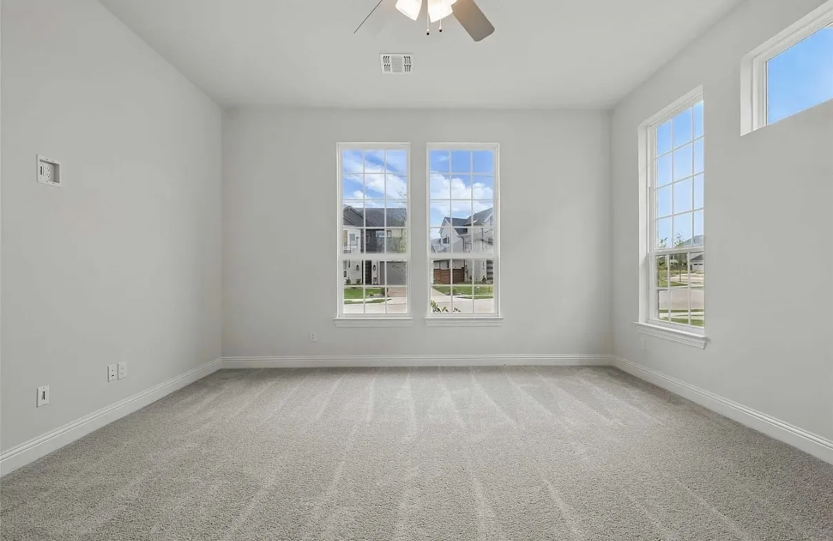 Spacious room featuring multiple windows, light gray carpeting, crisp white walls, and a ceiling fan