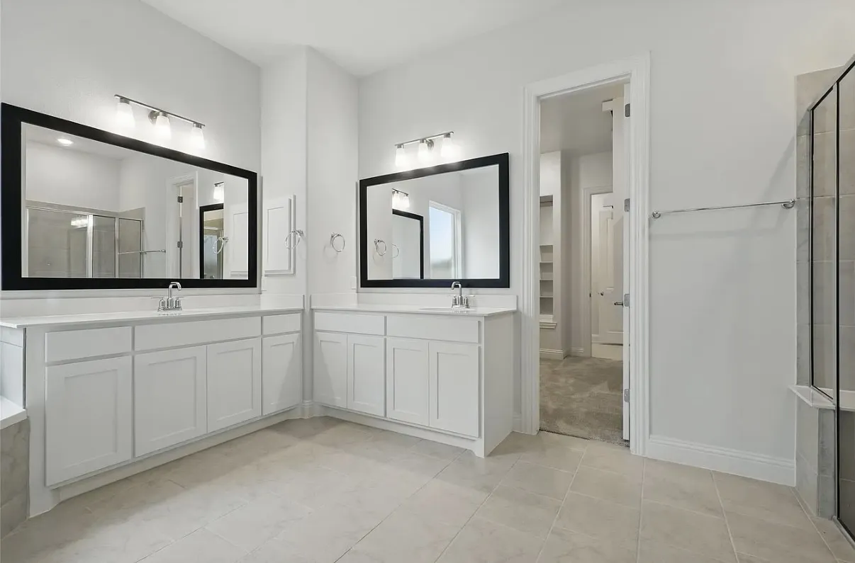 Spacious bathroom featuring dual vanities with white cabinetry and light countertops, framed mirrors, and tile flooring