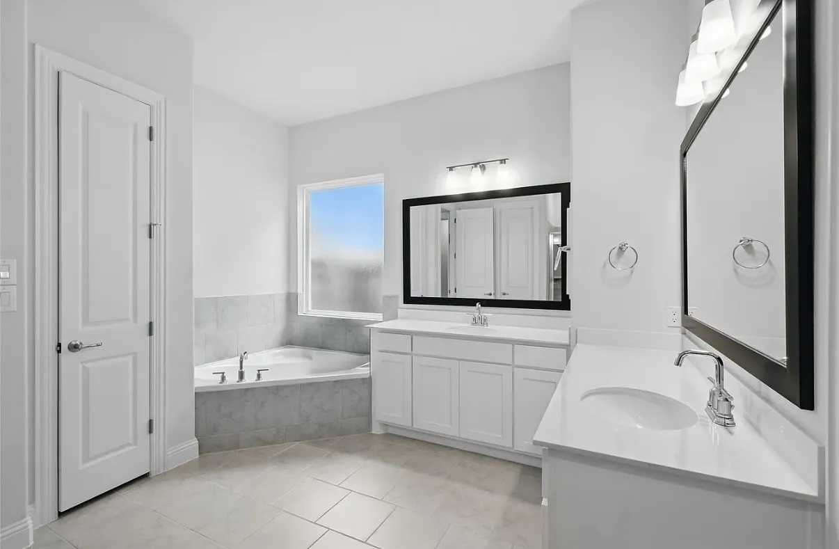 Bathroom with a built-in corner soaking tub, dual white vanities with integrated sinks, and individual framed mirrors