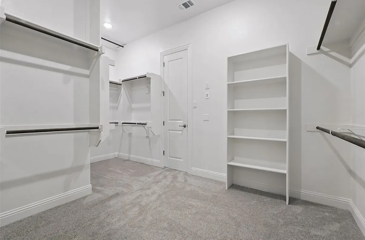 Spacious walk-in closet featuring light gray carpet, white walls, and extensive built-in shelving and hanging rods