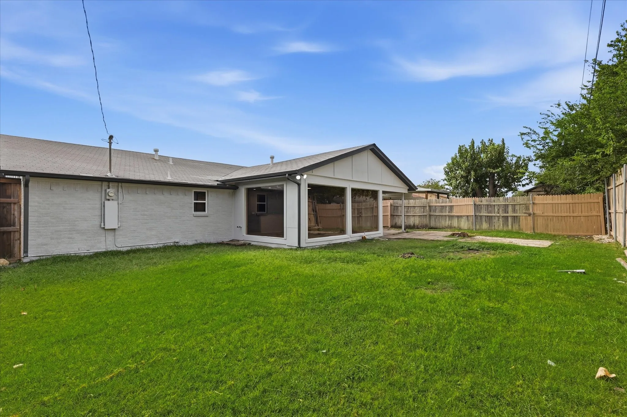 Spacious backyard featuring a sunroom addition with large windows, a fenced perimeter, and a substantial lawn area