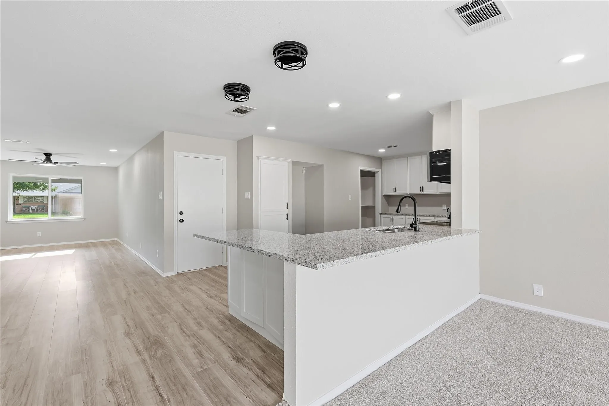 Open-concept kitchen and living area featuring a breakfast bar with a stone countertop, light wood-finish flooring, recessed lighting, and a ceiling fan