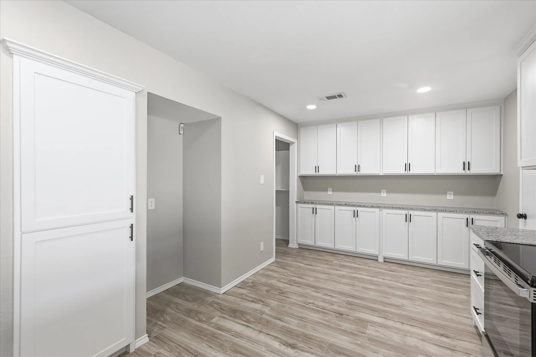 Light wood-finish flooring complements abundant white cabinetry and granite-pattern countertops